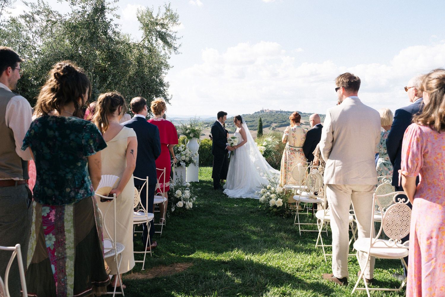 Guests watching bride and groom exchange vows at elegant outdoor Tuscan countryside wedding ceremony.