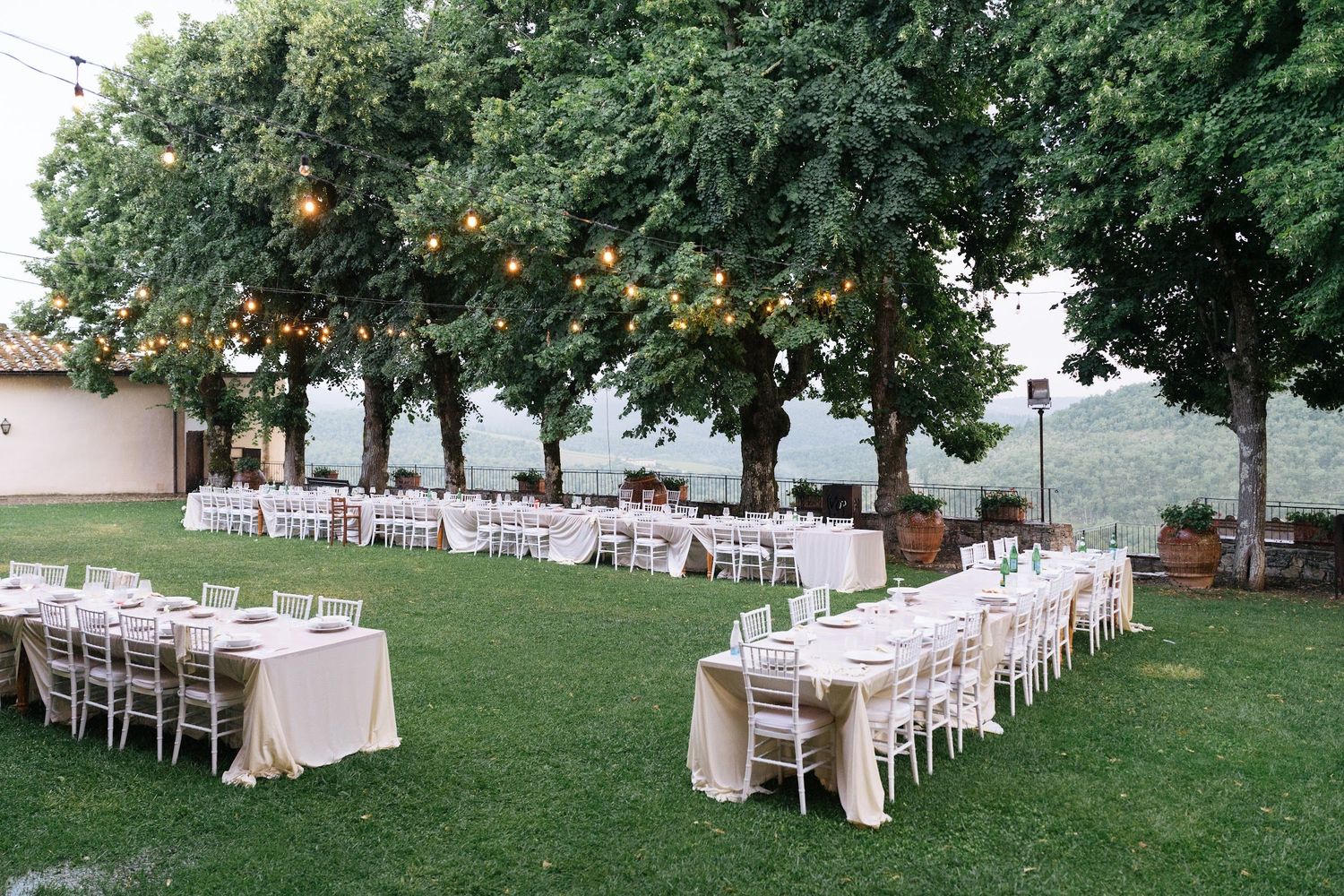 Elegant outdoor wedding reception with long tables, string lights, and lush green trees.