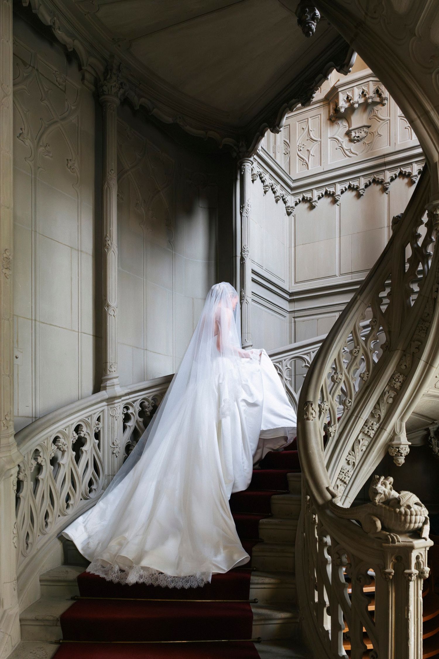 Bride ascending stunning gothic spiral staircase in dramatic flowing white wedding gown and veil.