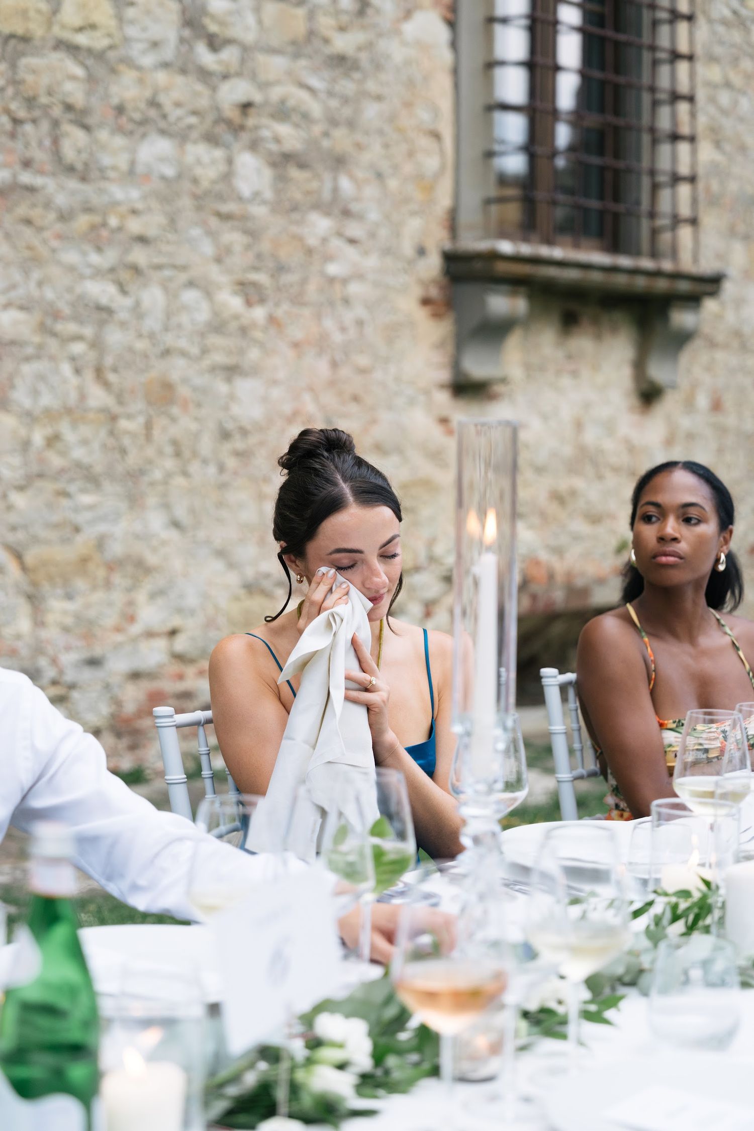 Emotional wedding guest dabs tears with a napkin during heartfelt speeches at an Italian reception.