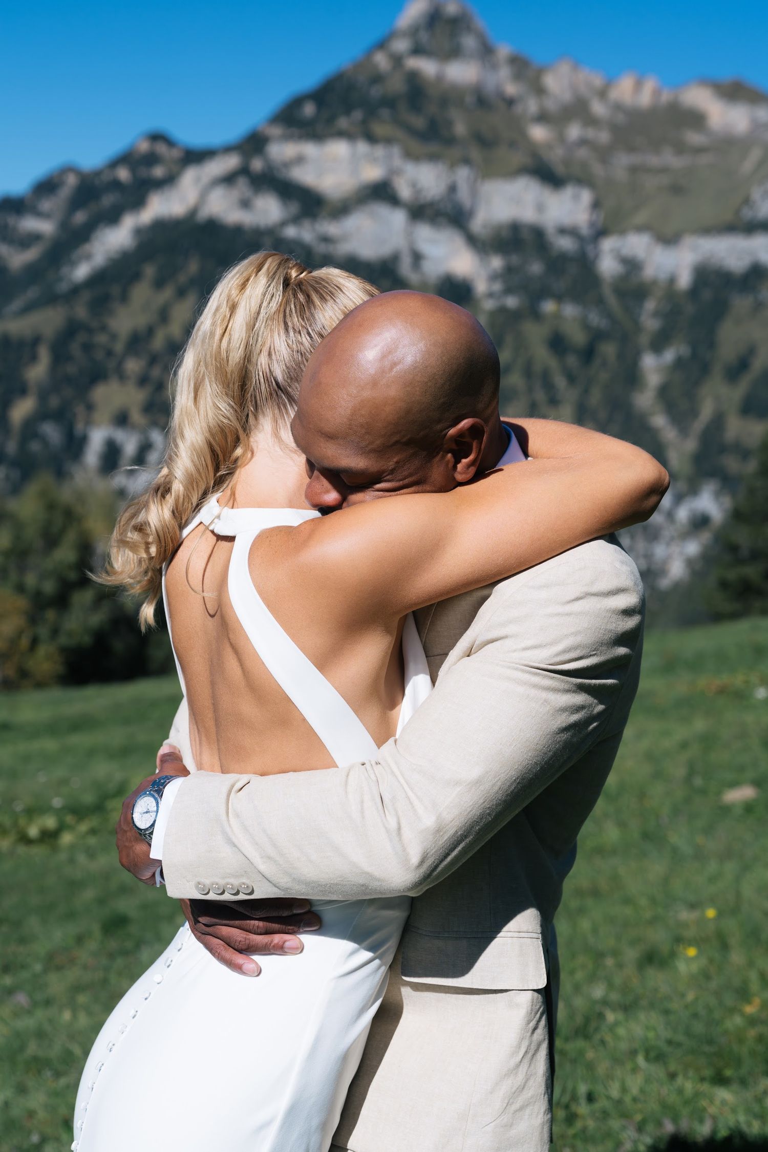 A couple embraces in wedding attire with a stunning Swiss Alps backdrop on a sunny day.
