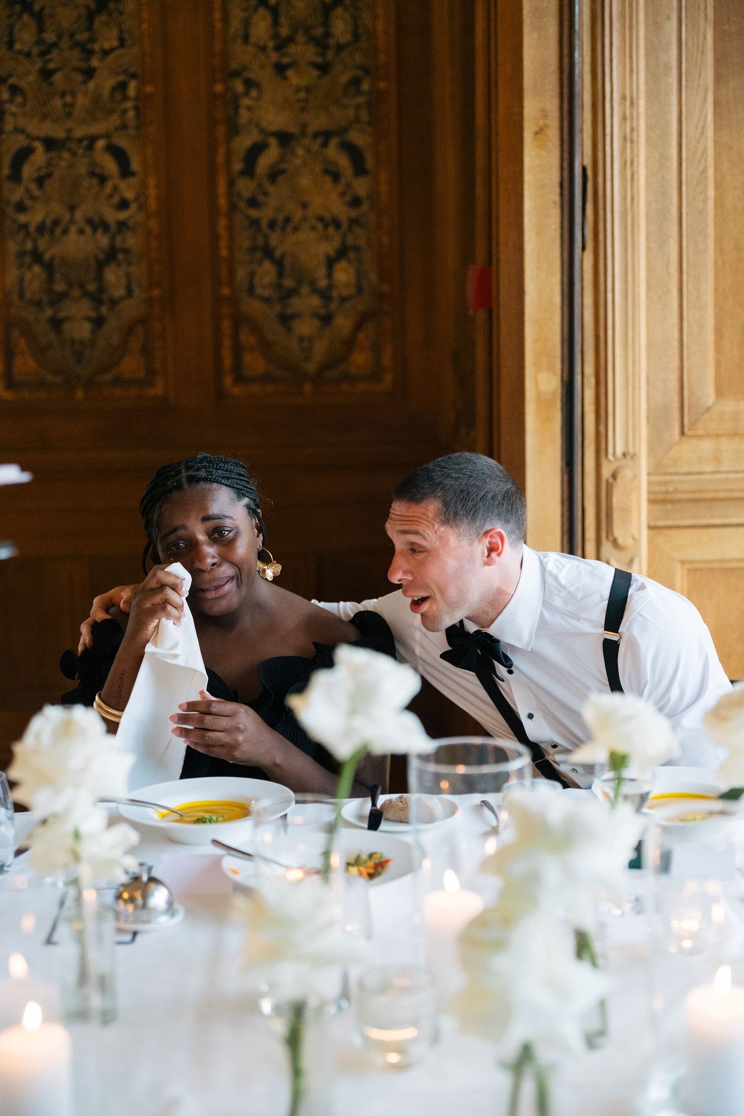 Wedding guests share a joyful moment together at a candlelit reception with white rose centerpieces.