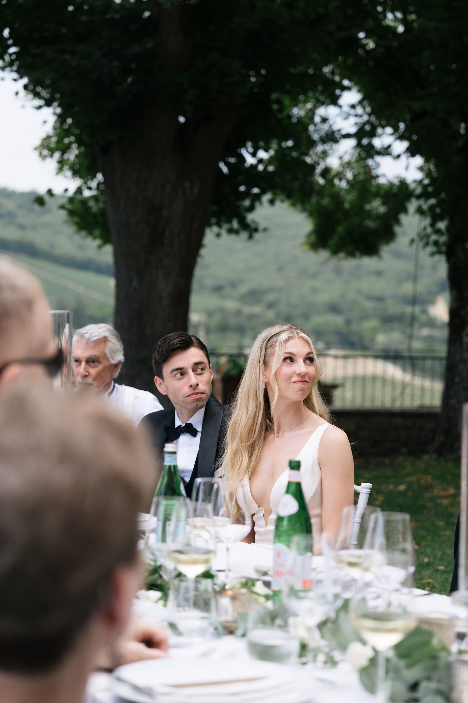 Bride and groom listen attentively to wedding speeches at an elegant outdoor Tuscan reception dinner.