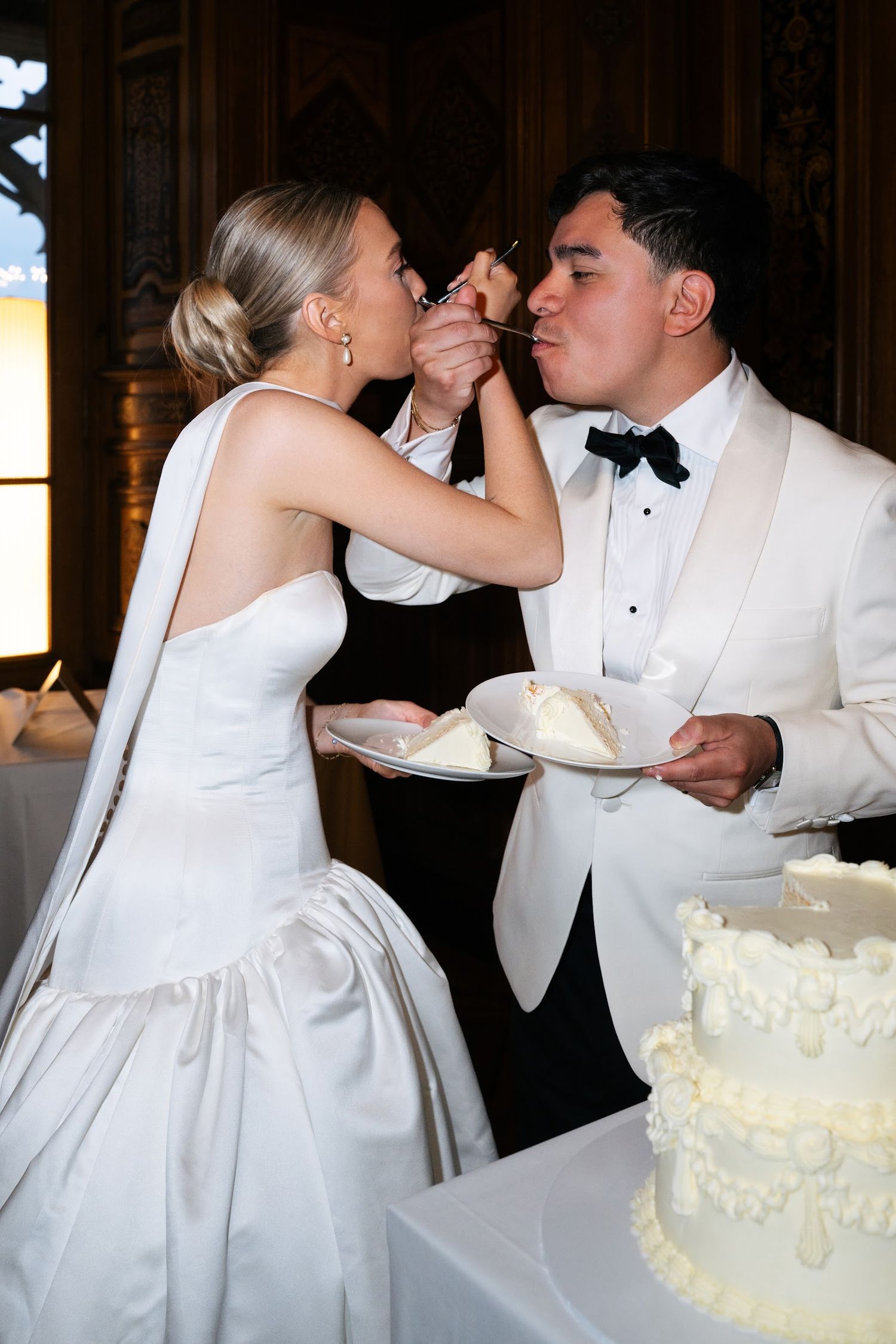 Bride feeding groom a bite of white wedding cake during their elegant reception celebration.