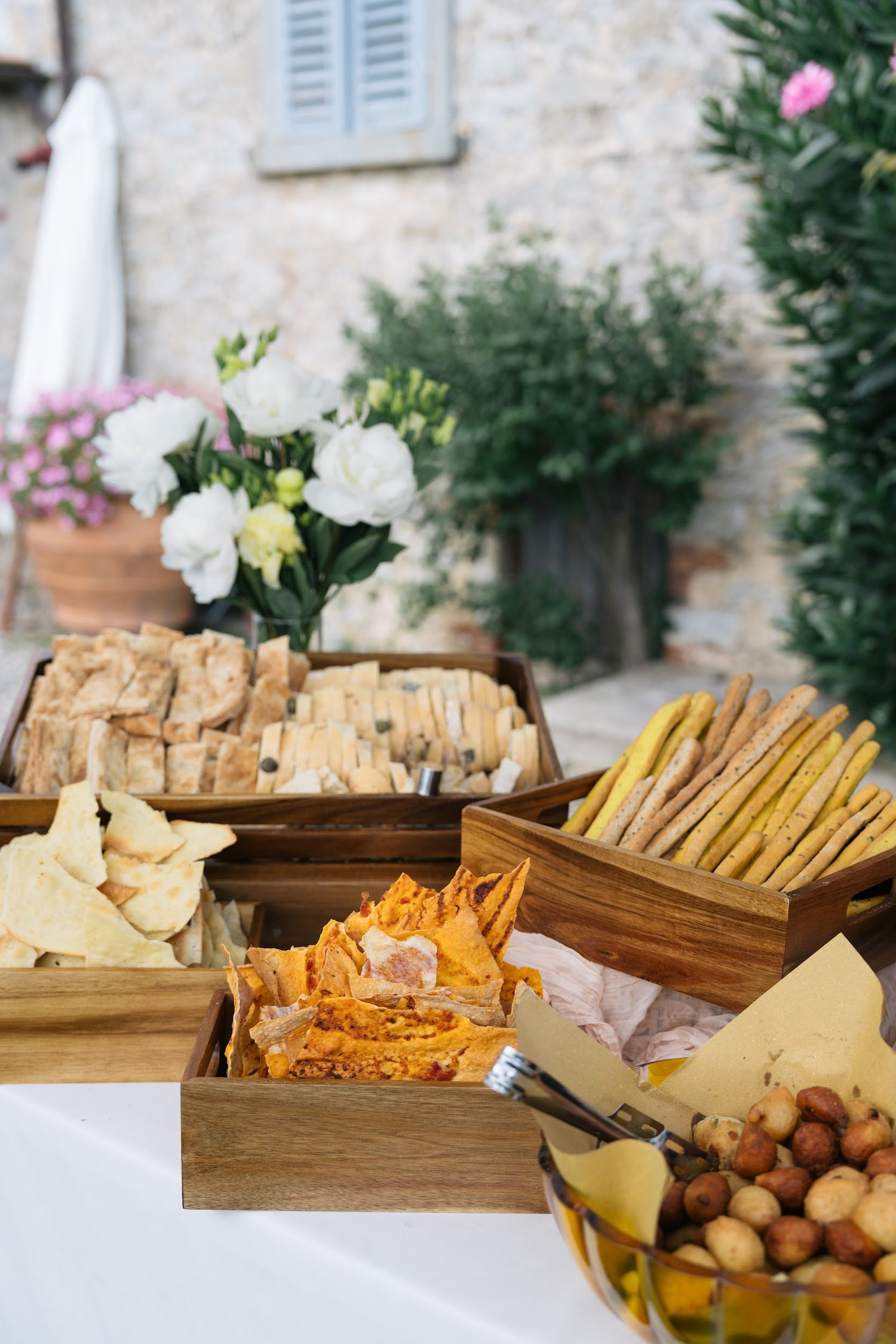 Elegant outdoor Italian wedding appetizer table with breadsticks, crackers, cheese, and white floral arrangements.