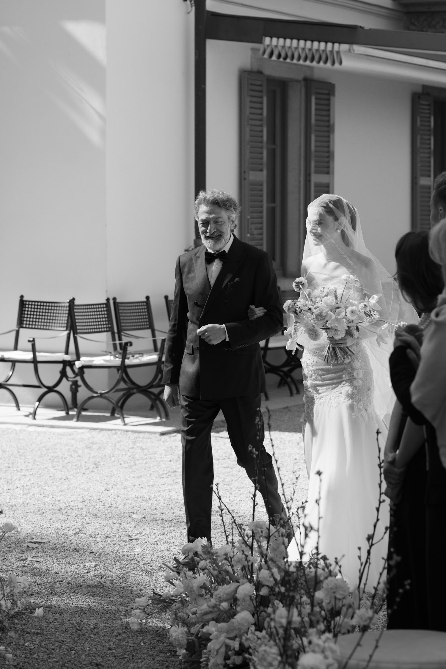 Black and white photo of bride in fitted gown walking down aisle with older gentleman.