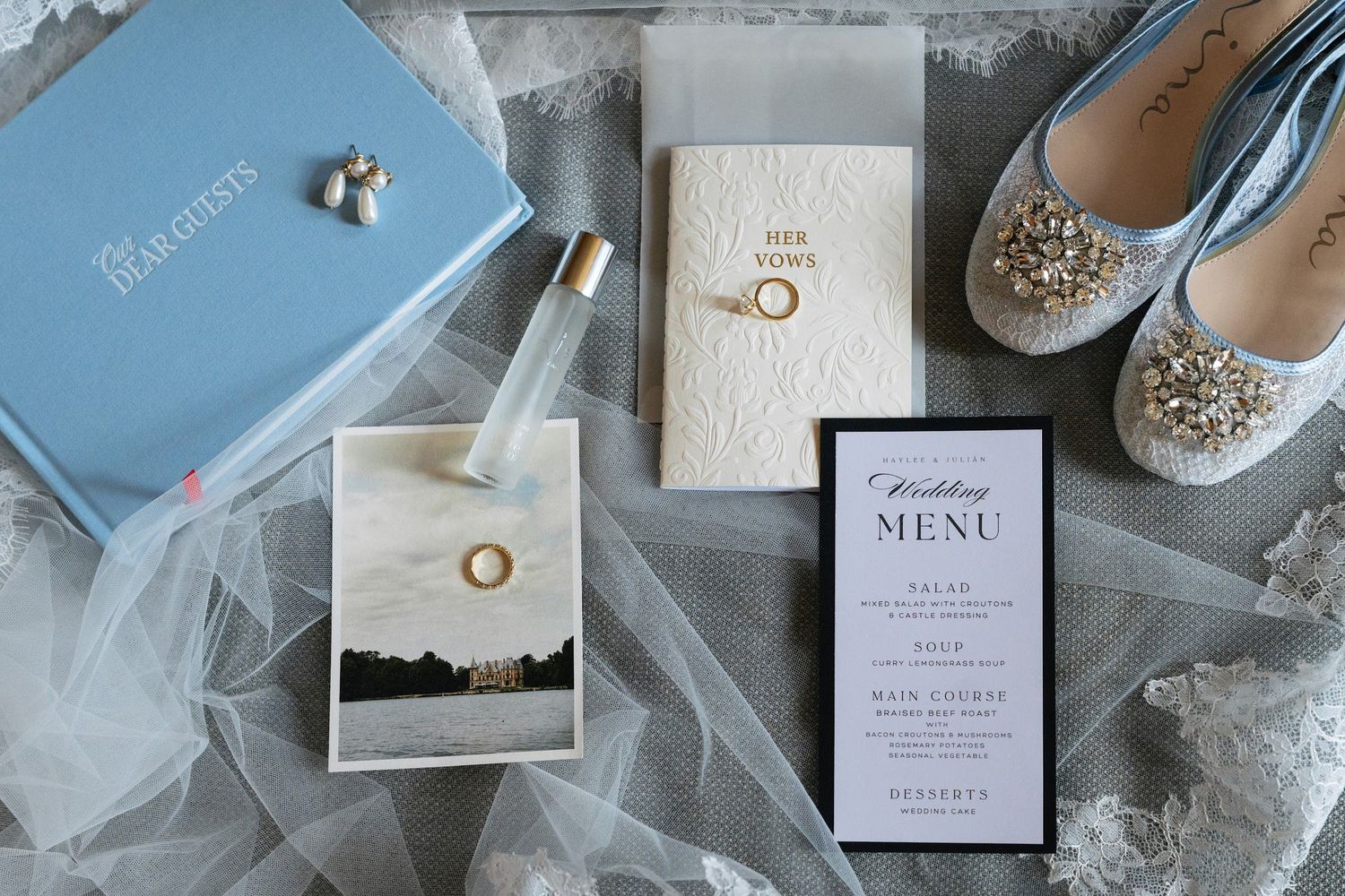 Flat lay of wedding details including rings, blue shoes, perfume, vow book, and elegant menu card.