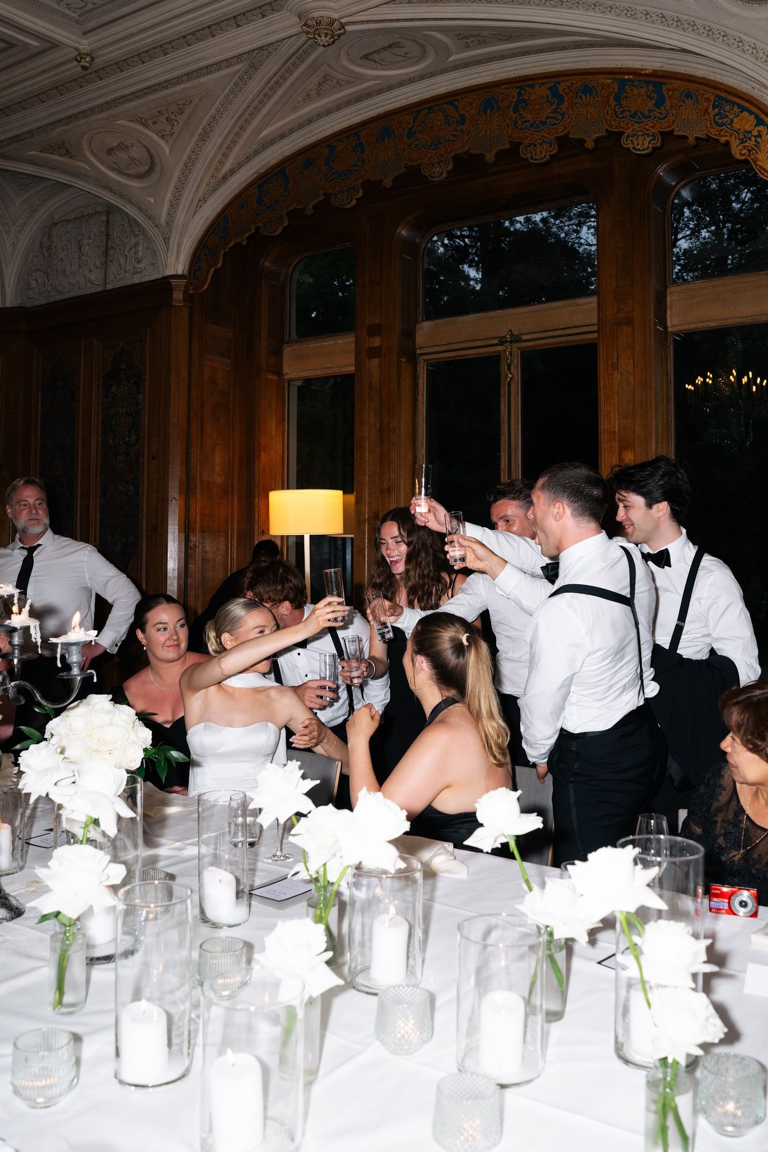Wedding party raises champagne glasses in a toast at elegant reception with white floral centerpieces.