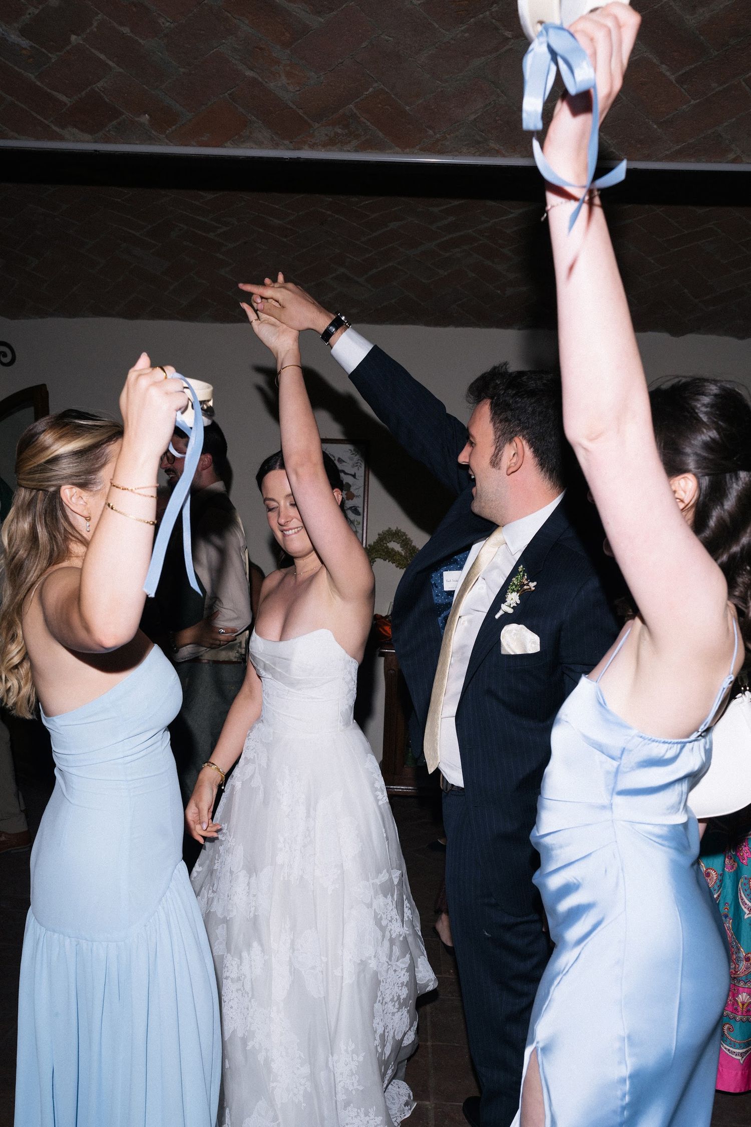 Bride, groom, and bridesmaids dance joyfully with raised ribbons at reception.