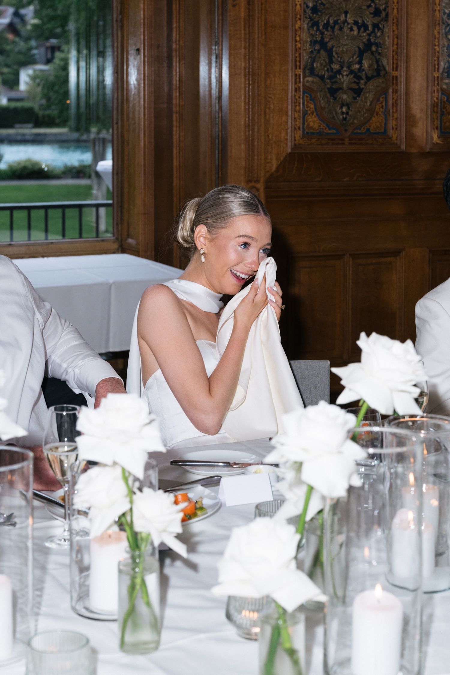 Emotional bride wiping tears at elegant wedding reception with white roses and candlelight.