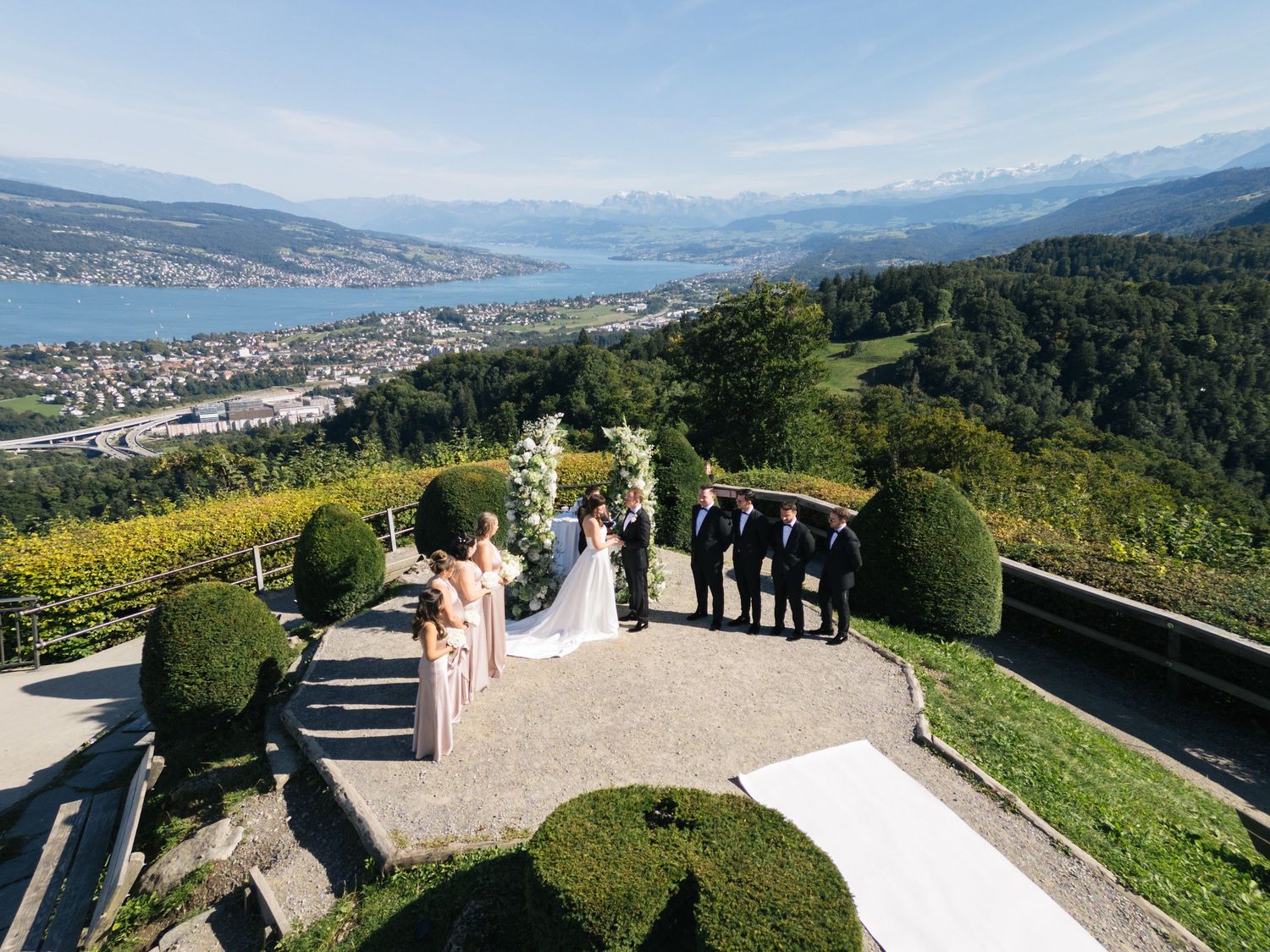 Aerial view of a wedding ceremony on a terrace overlooking a stunning Swiss lake and mountain landscape.
