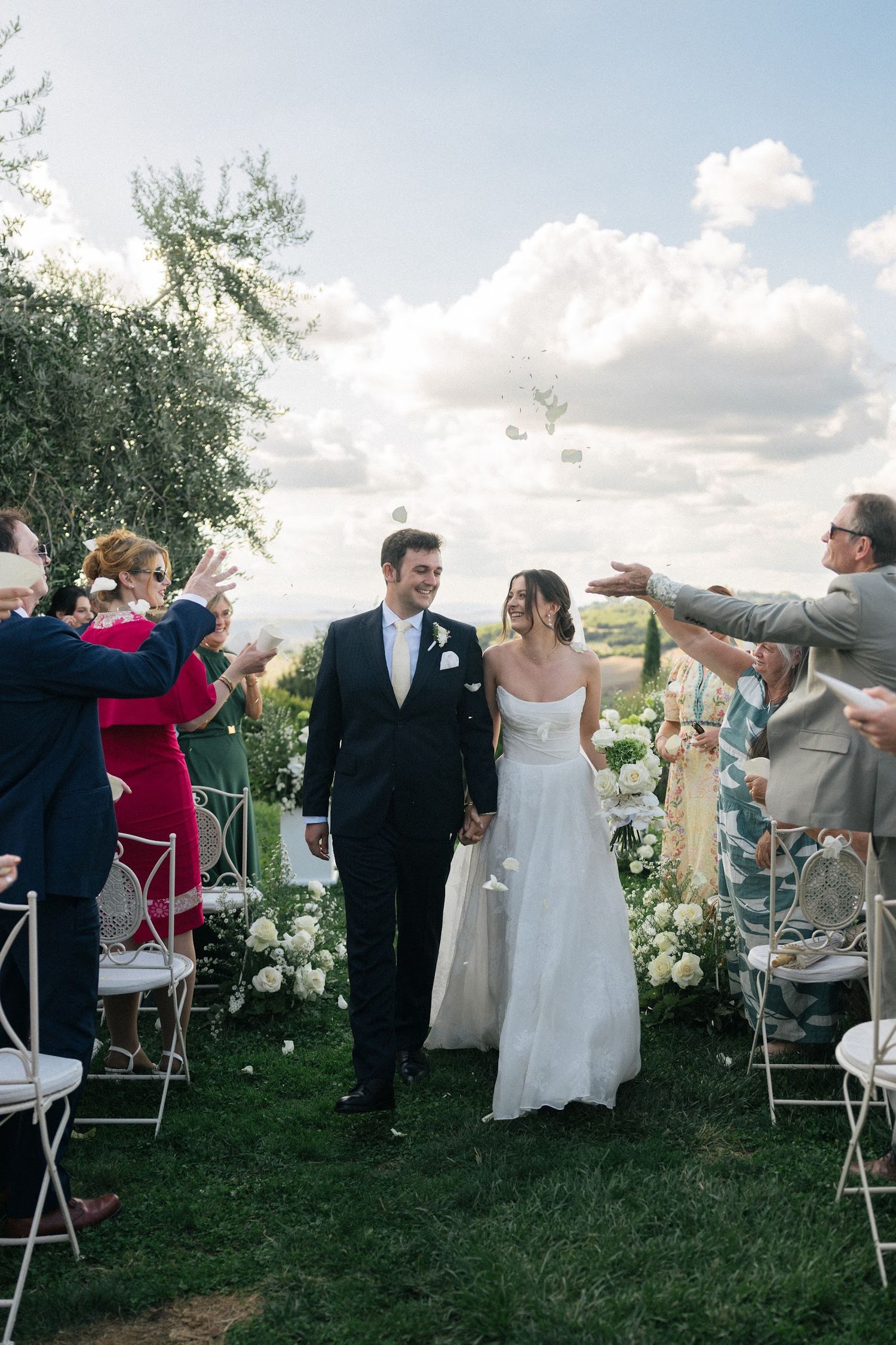 Newlyweds walk down aisle as guests toss petals during outdoor Tuscan wedding ceremony.