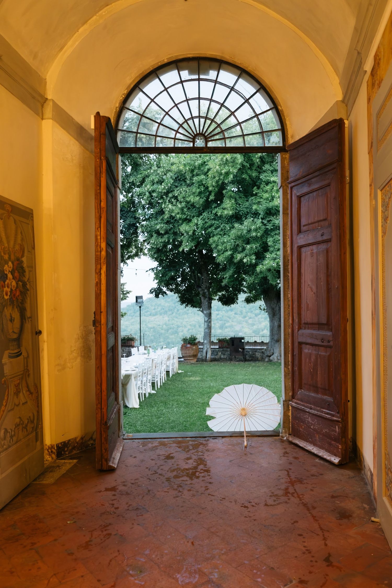 View through ornate arched doorway of outdoor wedding reception setup with white parasol.