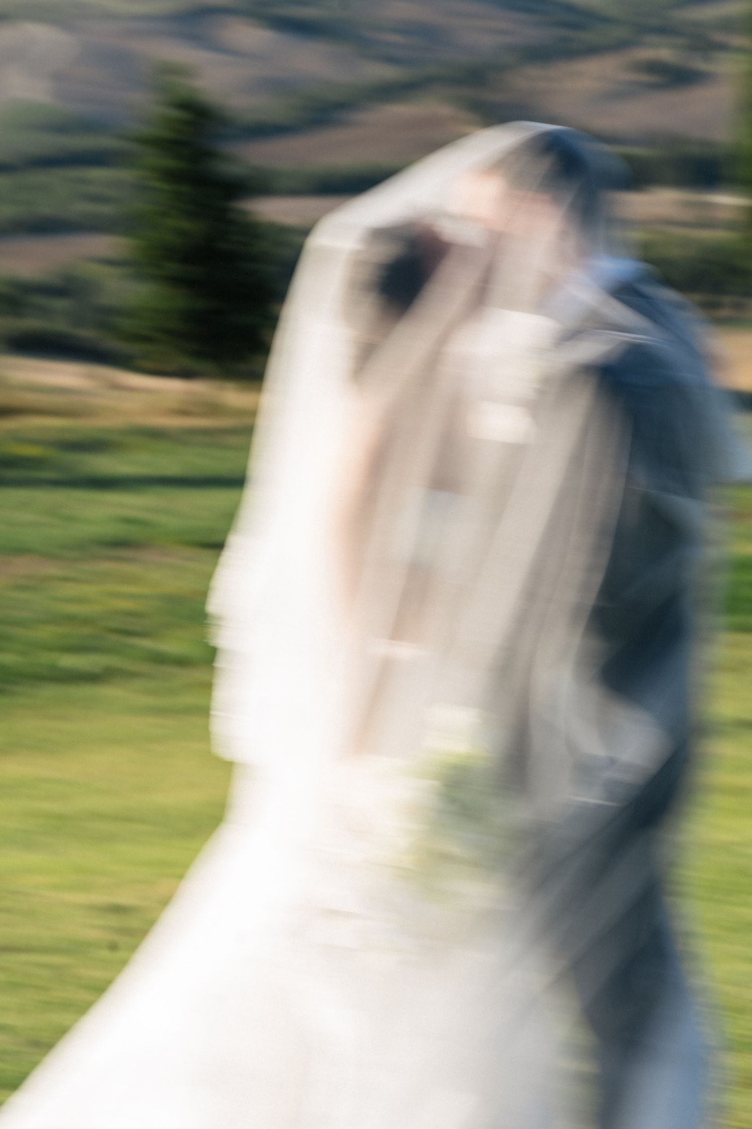 Artistic motion blur photo of bride and groom kissing under veil in Tuscan landscape.