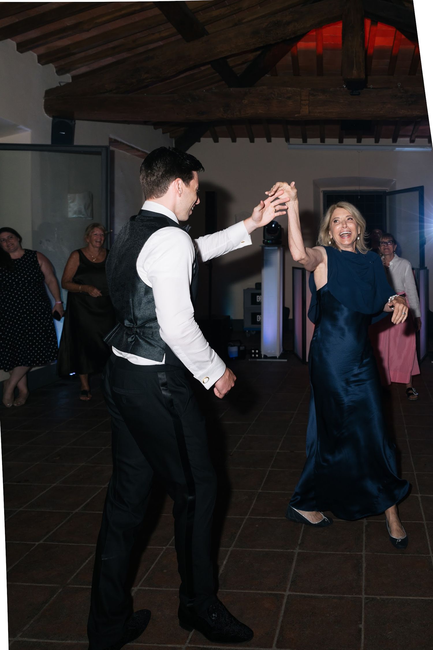 Groom in black vest dancing with a woman in an elegant navy blue gown at the wedding reception.