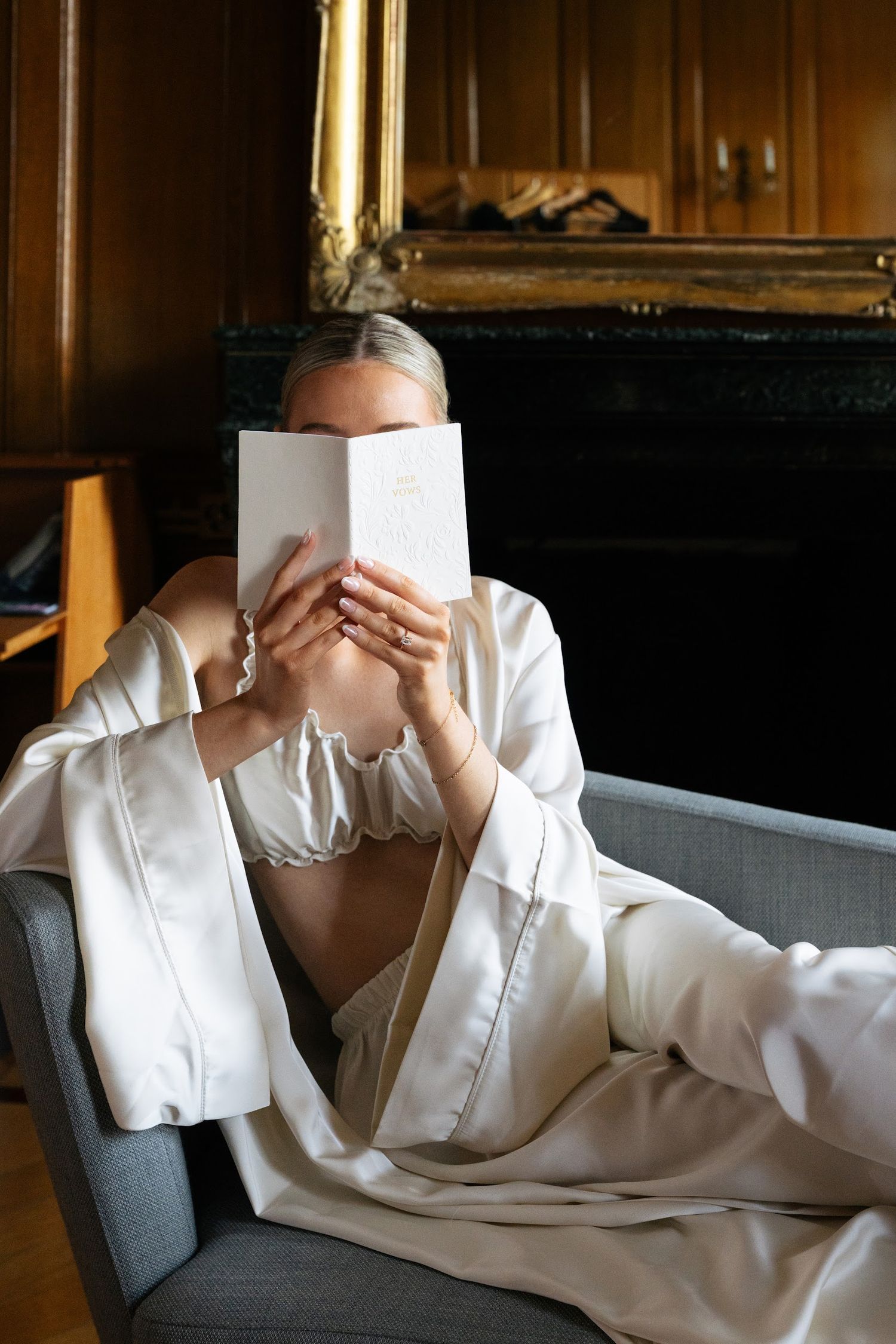 Elegant bride in a silk robe relaxing on a sofa while reading her wedding vows in a luxurious room.