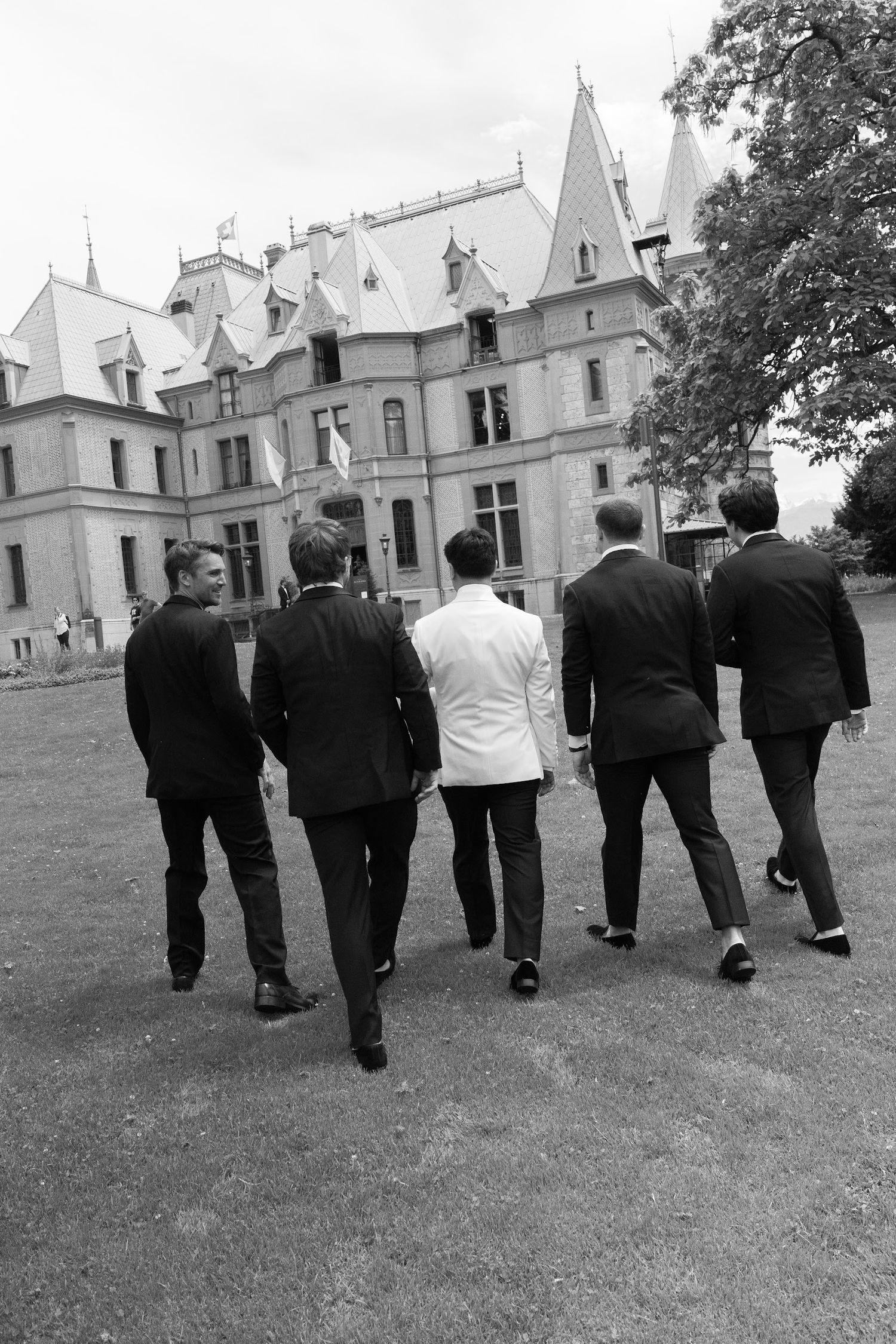 Black and white photo of groom and groomsmen walking toward grand castle wedding venue.
