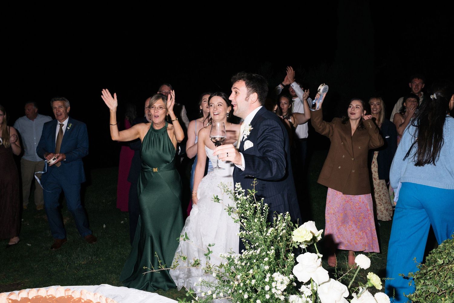 Bride and groom celebrate with guests during outdoor evening wedding reception.