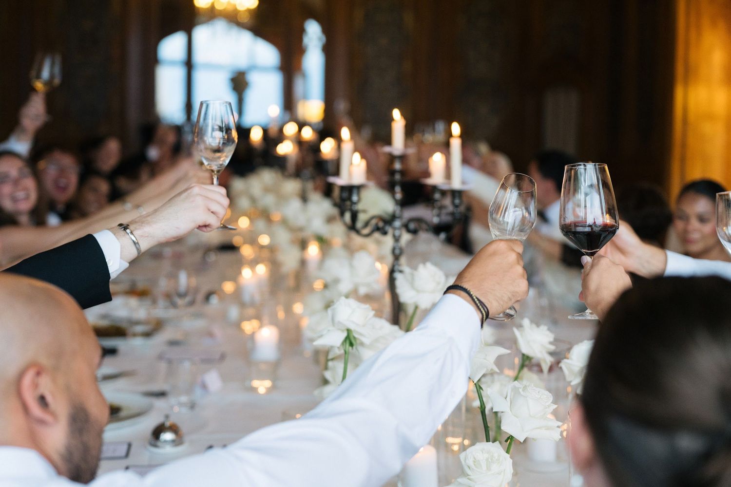 Wedding guests raising glasses in a champagne toast at a candlelit reception banquet.