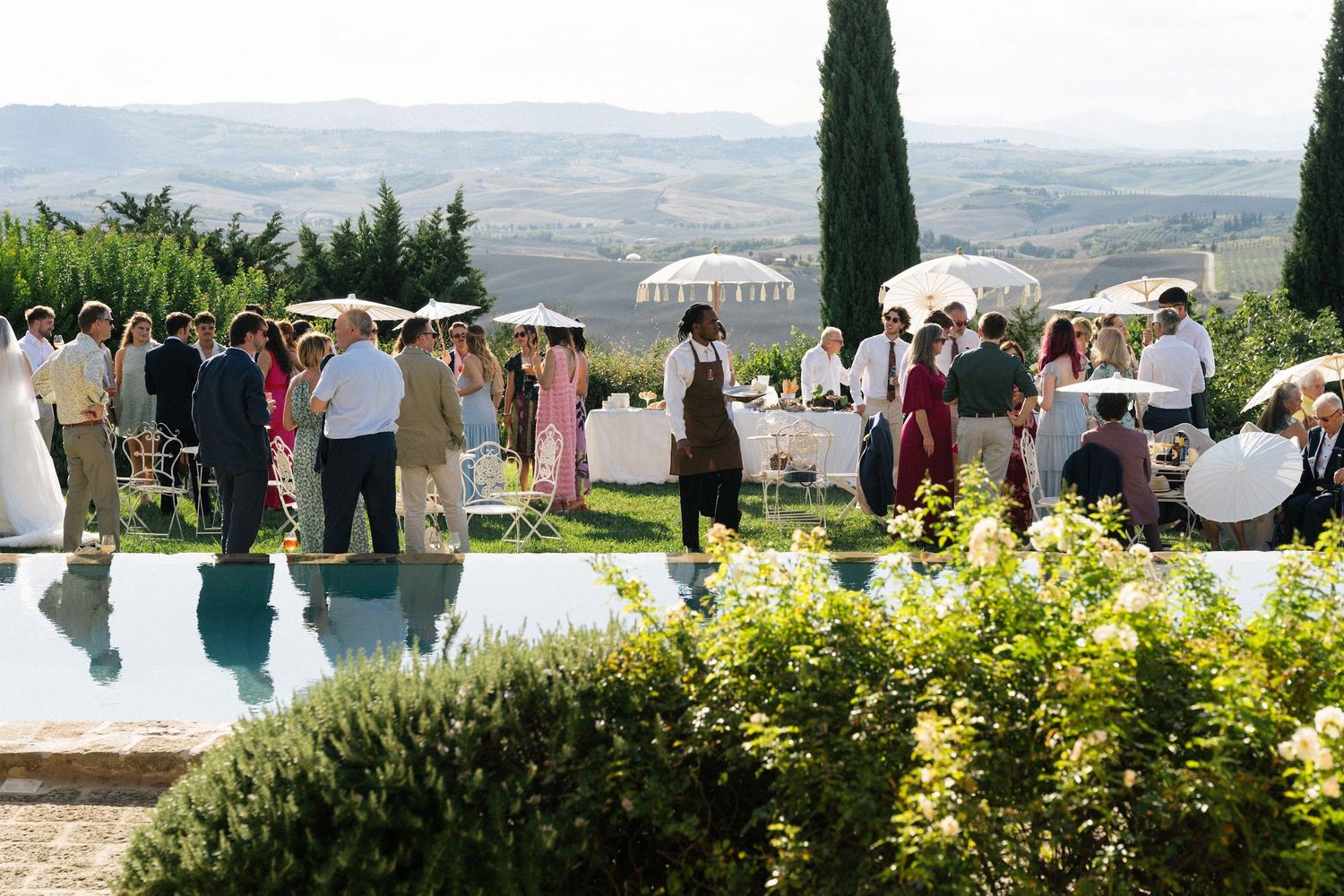 Elegant outdoor wedding reception by poolside with rolling Tuscan hills and cypress trees backdrop.
