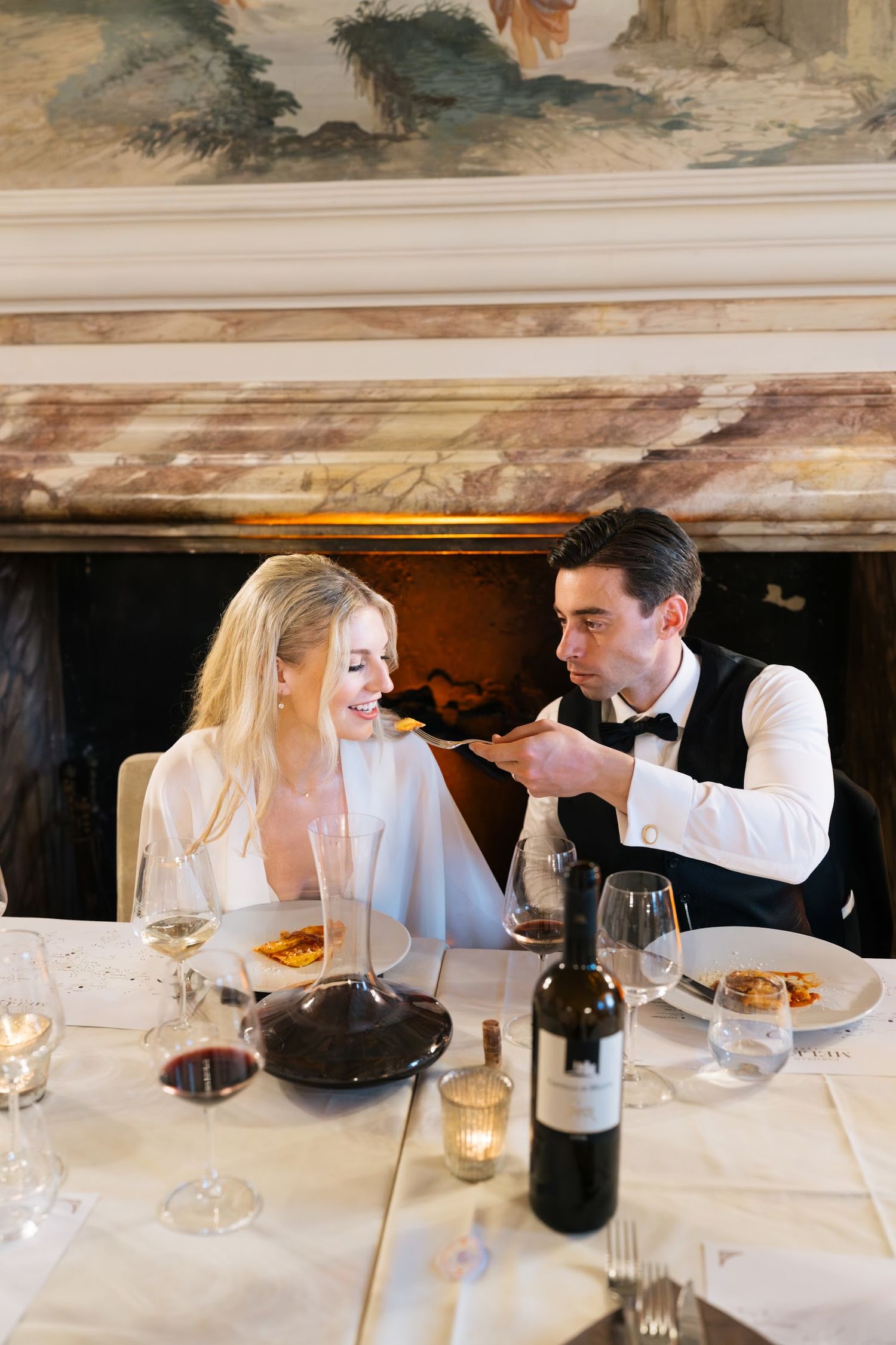 Groom feeding bride at elegant Italian castle wedding reception dinner with wine and candlelight.