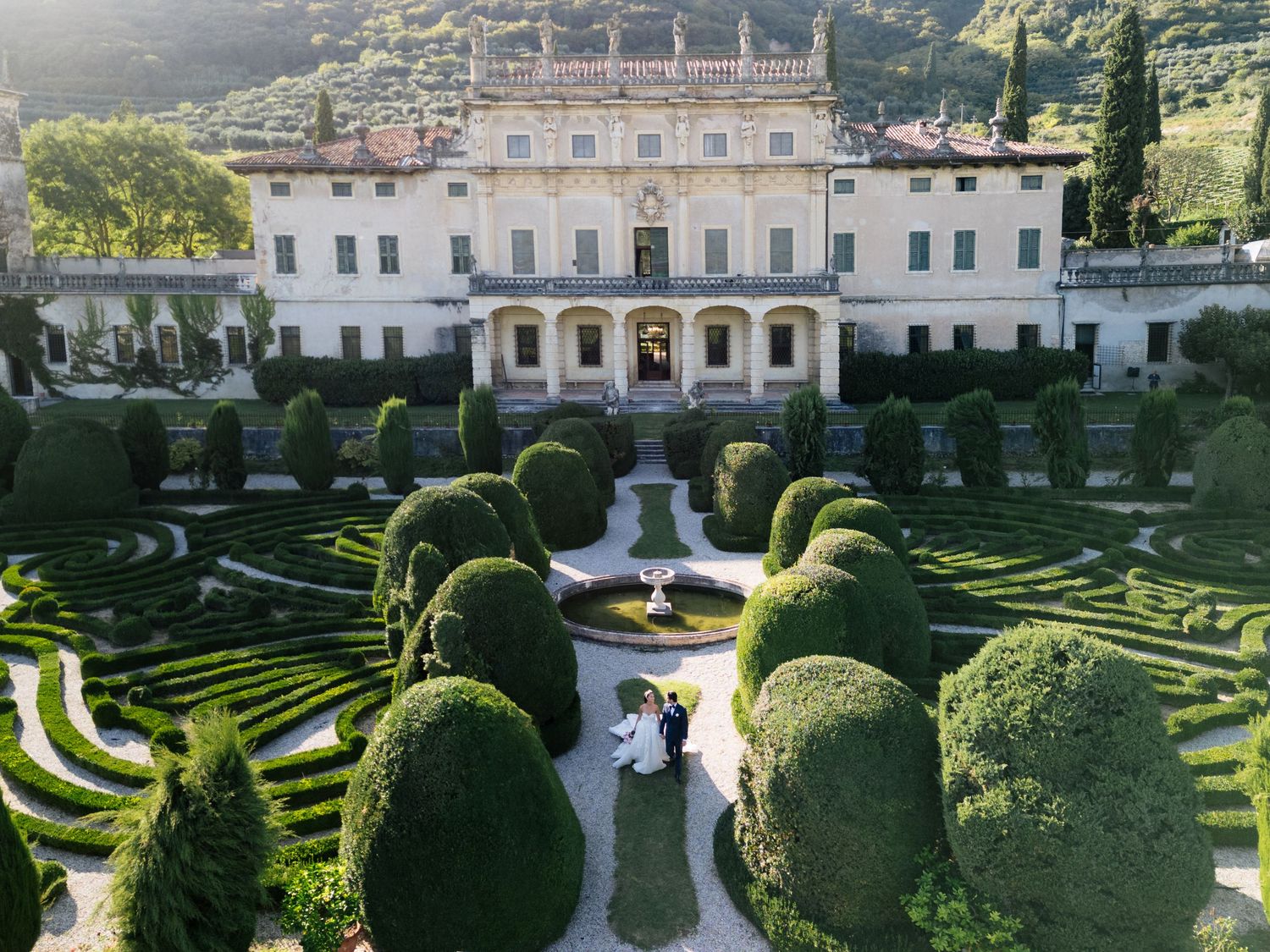 Aerial view of a couple embracing in the manicured gardens of a grand Italian villa wedding venue.