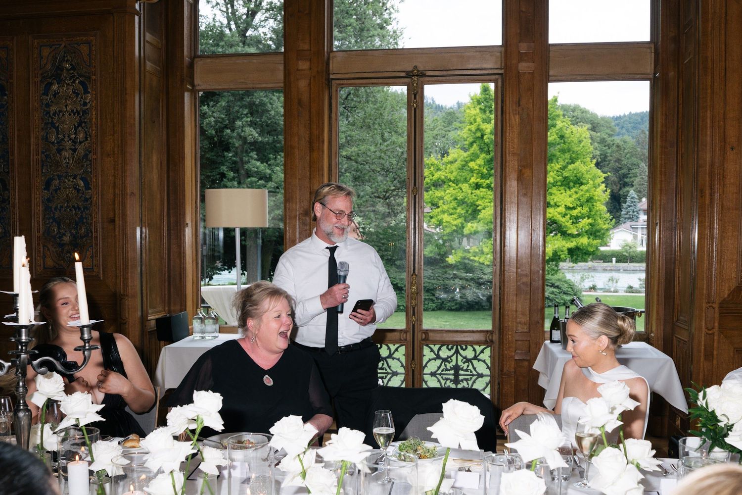 Man delivers a heartfelt speech with microphone at an elegant wedding reception dinner table.