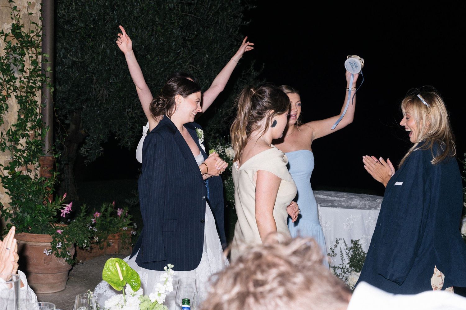 Bridesmaids celebrate with raised arms at an outdoor wedding reception.