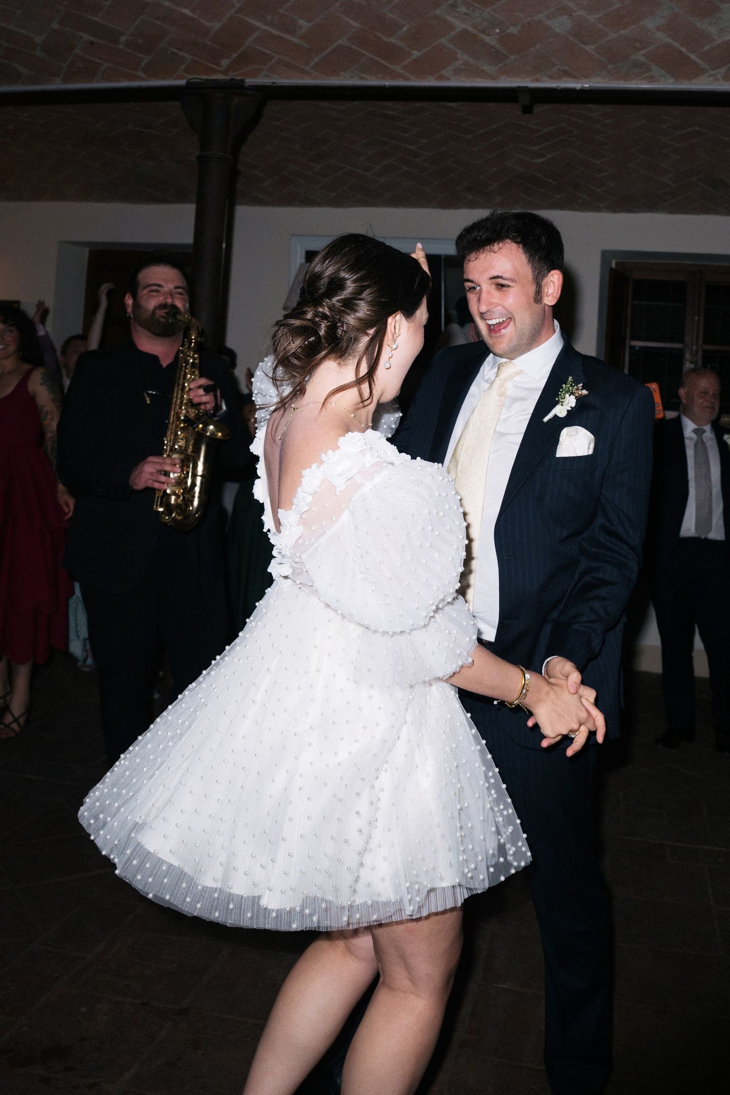 Groom smiling at bride in white pearl mini dress during wedding dance.