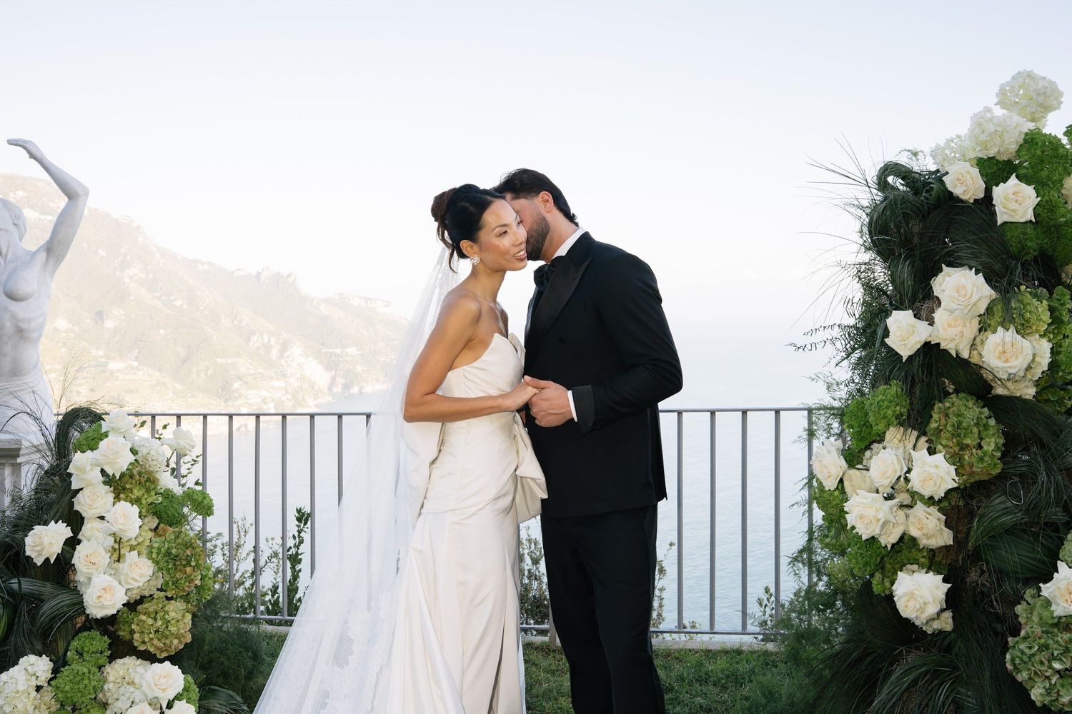 Couple shares a kiss at an outdoor ceremony with white hydrangeas and coastal mountain views.