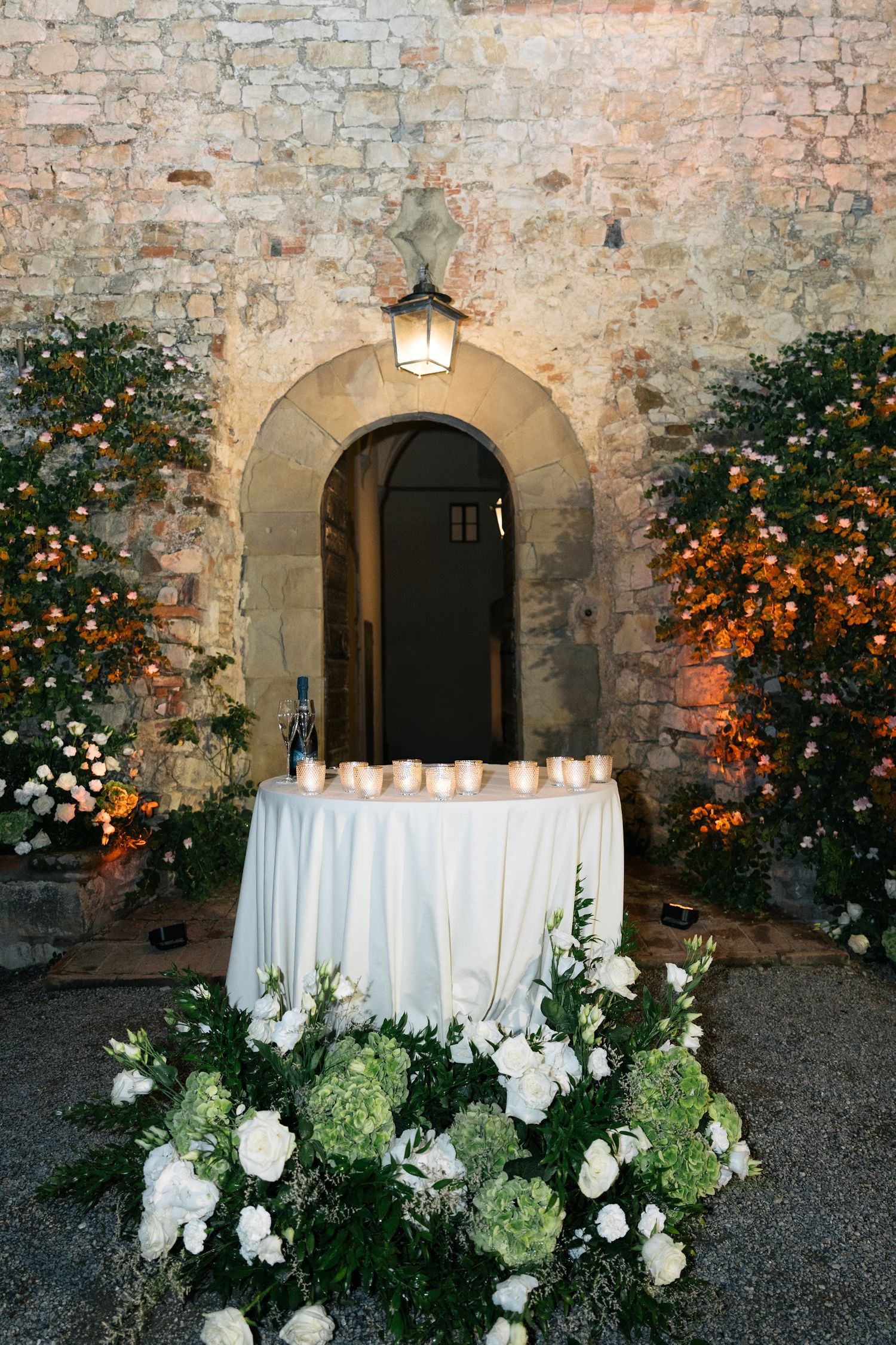 White floral arrangements and candles on draped sweetheart table at Italian castle wedding.