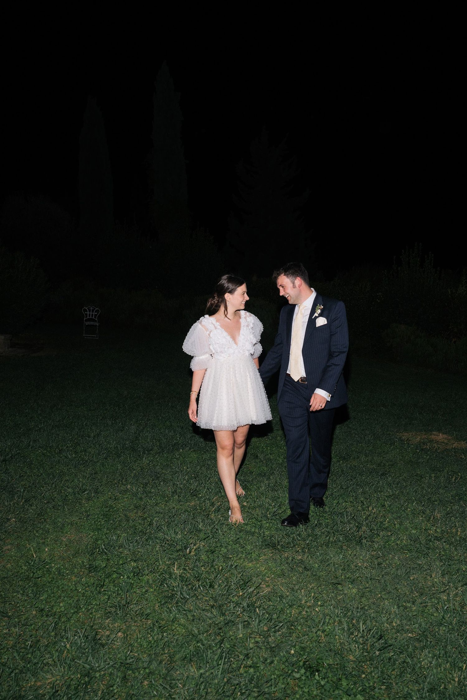 Bride and groom walking together on grass at night after wedding.