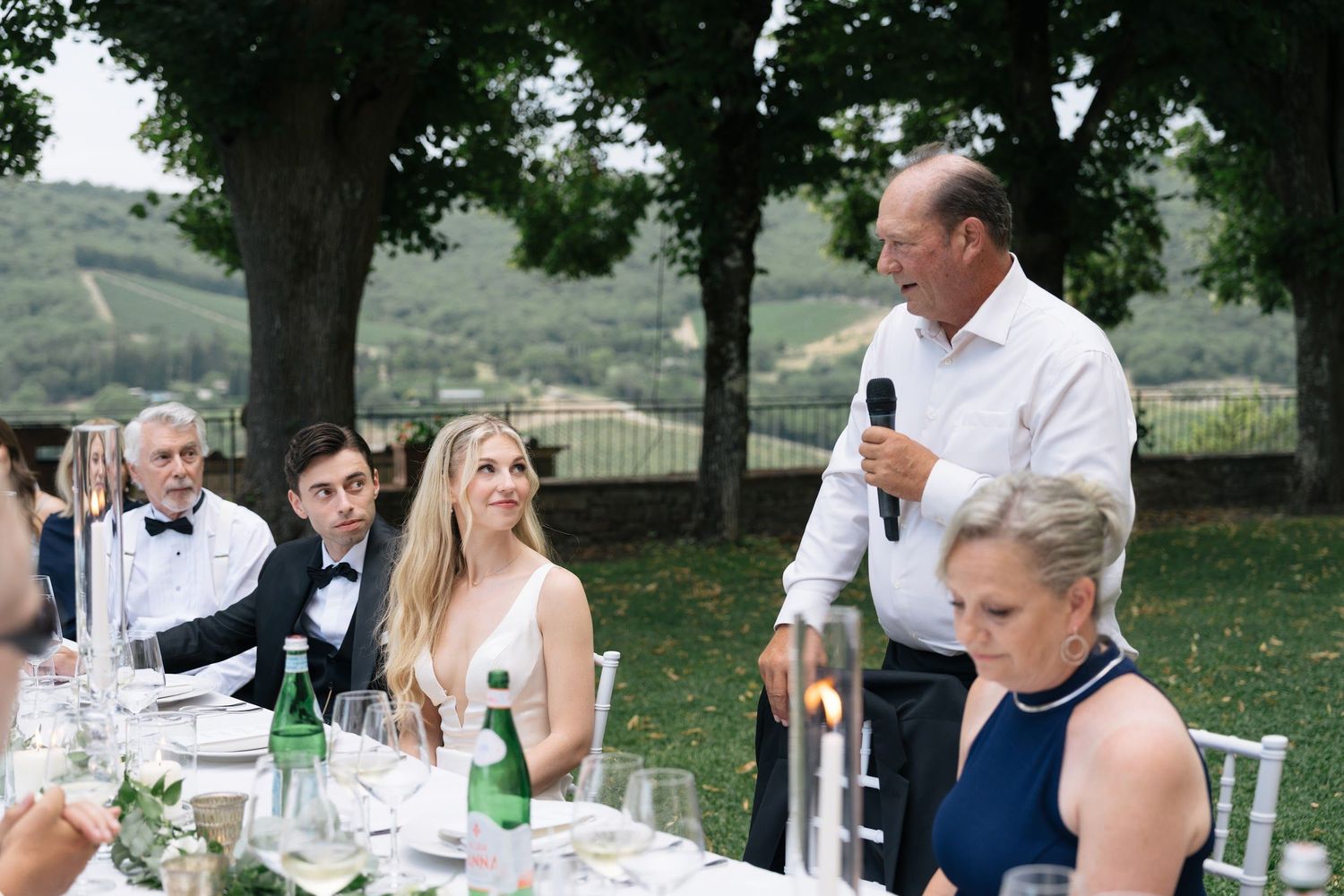Father of the bride delivers a heartfelt speech at an outdoor Tuscan wedding reception dinner.
