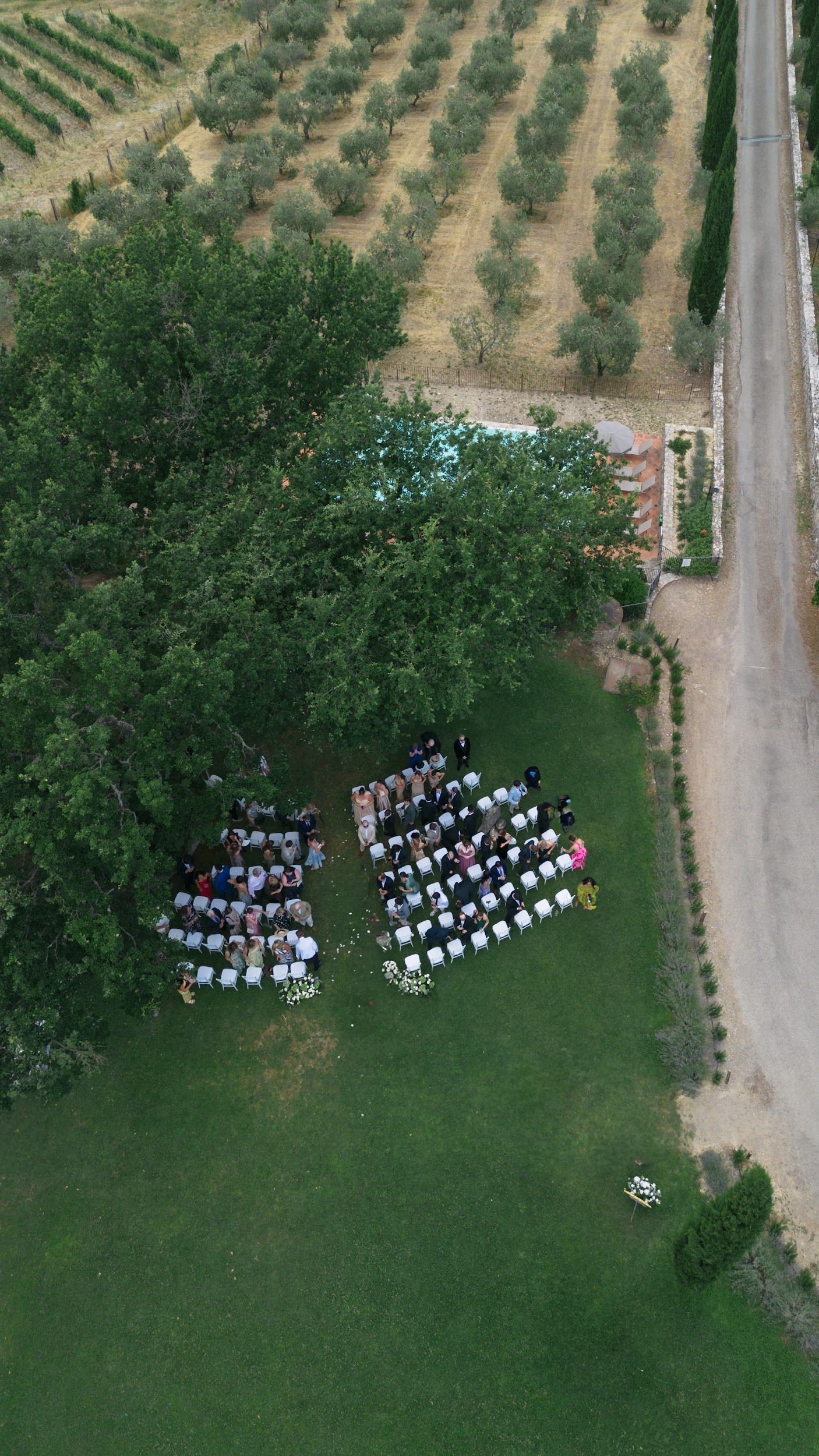 Aerial drone view of outdoor wedding ceremony with guests seated in rows on lush green lawn.