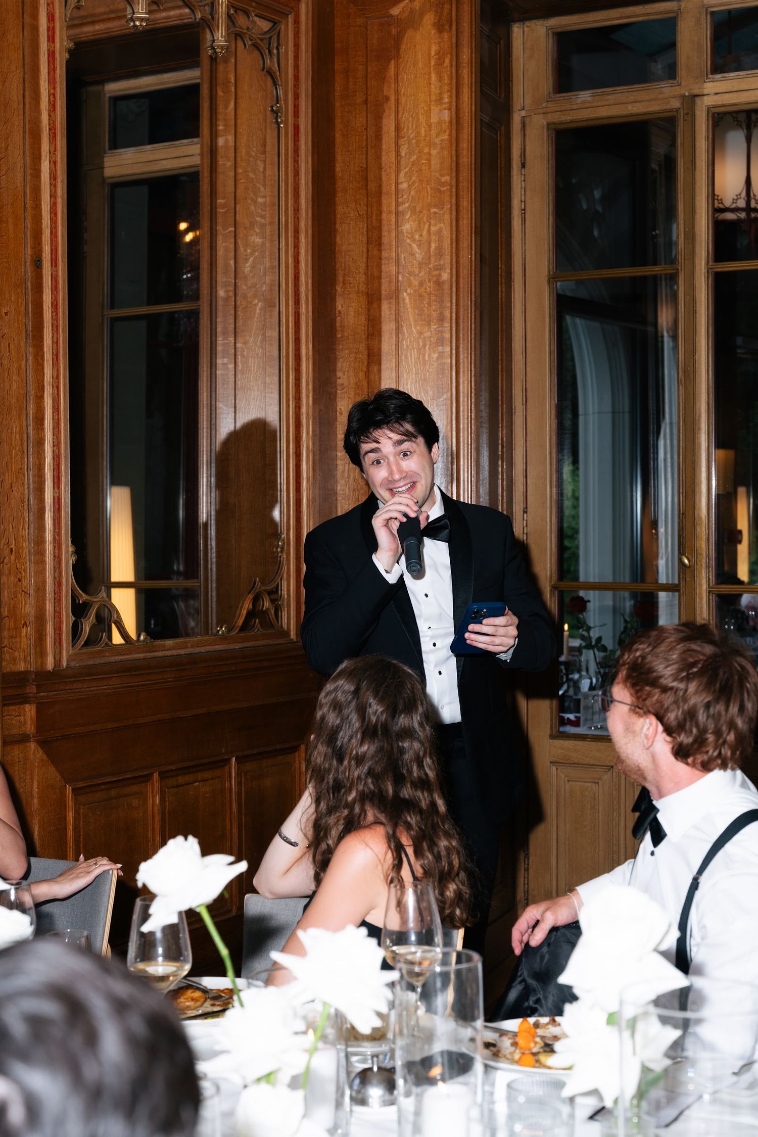 Best man delivers a heartfelt speech at wedding reception dinner in a classic wood-paneled venue.