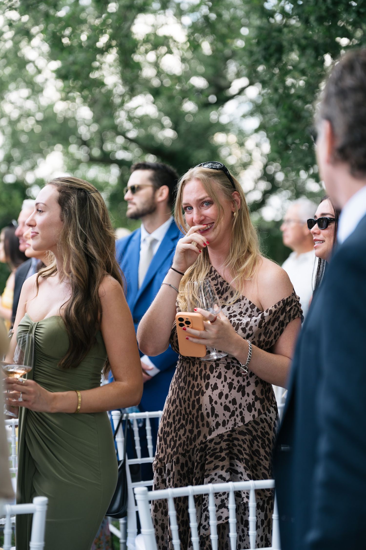 Guests laugh and mingle at an outdoor wedding cocktail hour, wearing elegant attire including a leopard print dress.