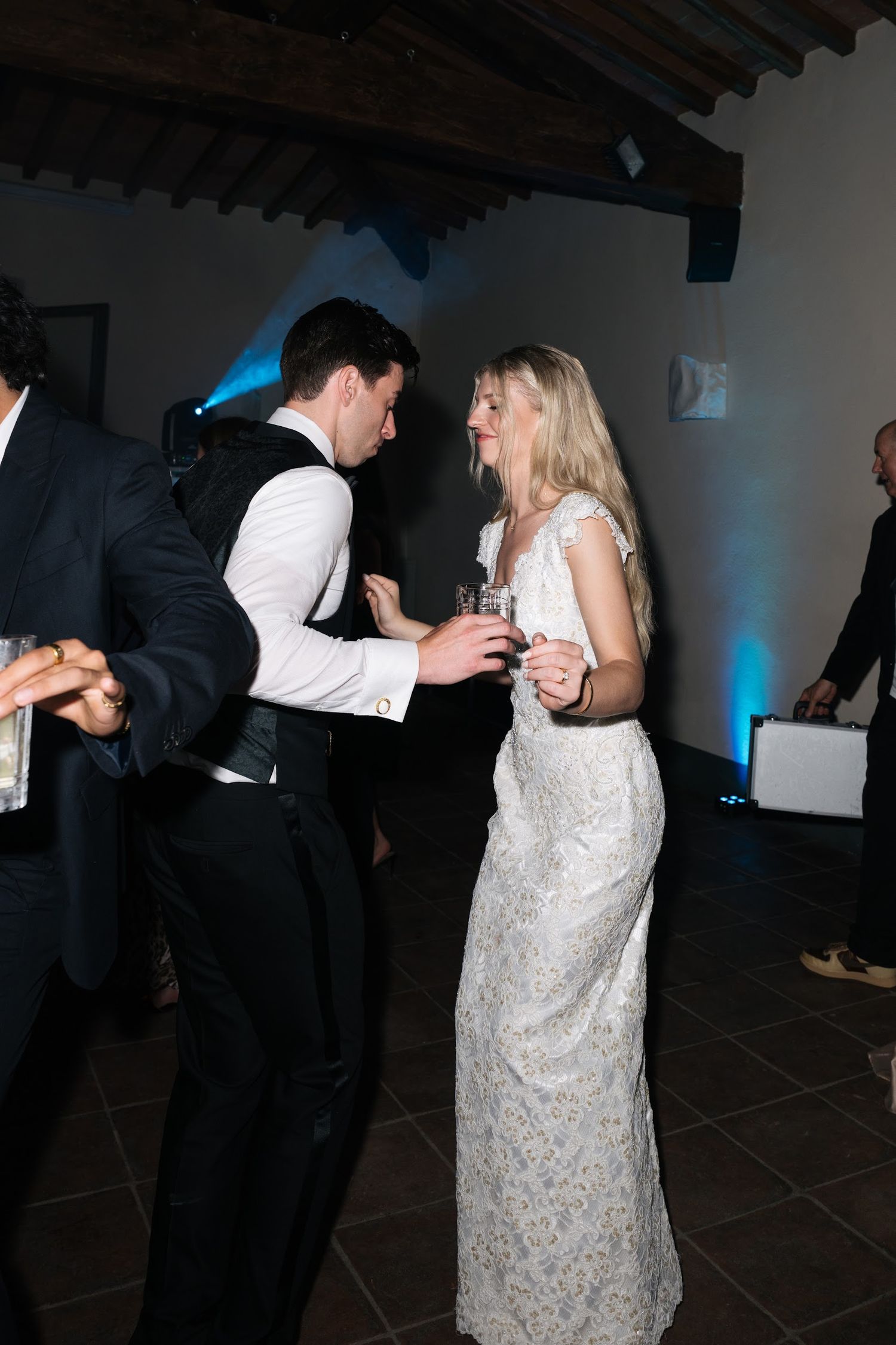Bride in lace gown and groom in vest dancing together at elegant wedding reception.