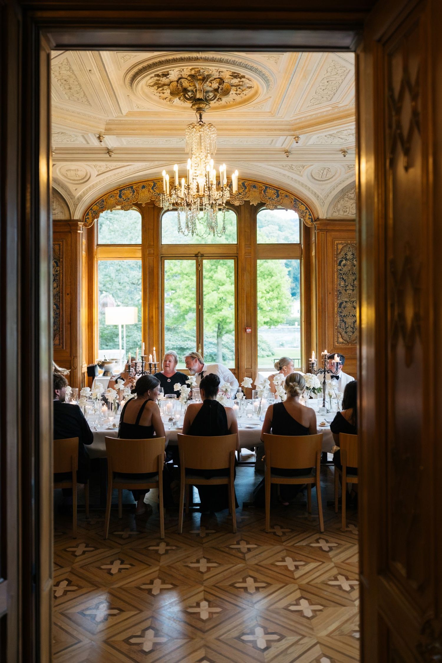 Elegant wedding reception room viewed through doorway featuring chandelier and ornate wood-paneled walls.