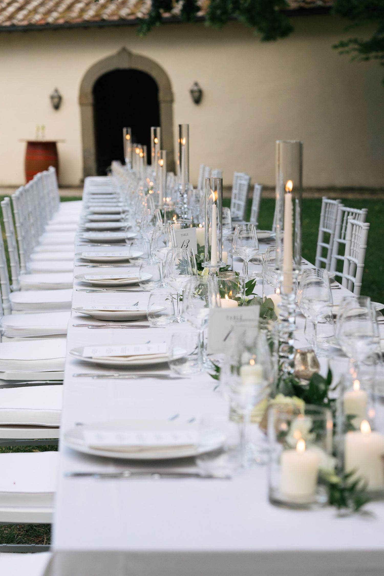 Long elegantly set wedding reception table with white linens, candles, and greenery centerpieces.