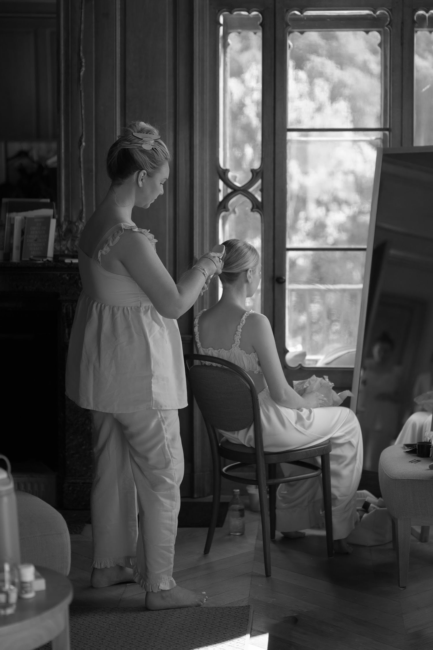 Black and white photo of a bridesmaid styling the brides hair by a ornate window in a historic villa.