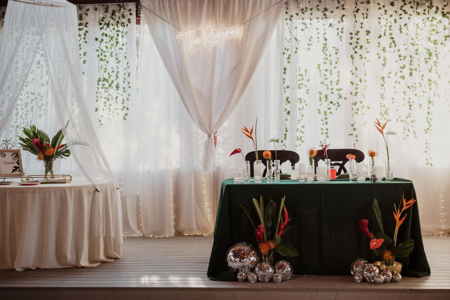 Elegant wedding reception setup with floral arrangements, draped curtains, and a decorated sweetheart table with tropical flowers.