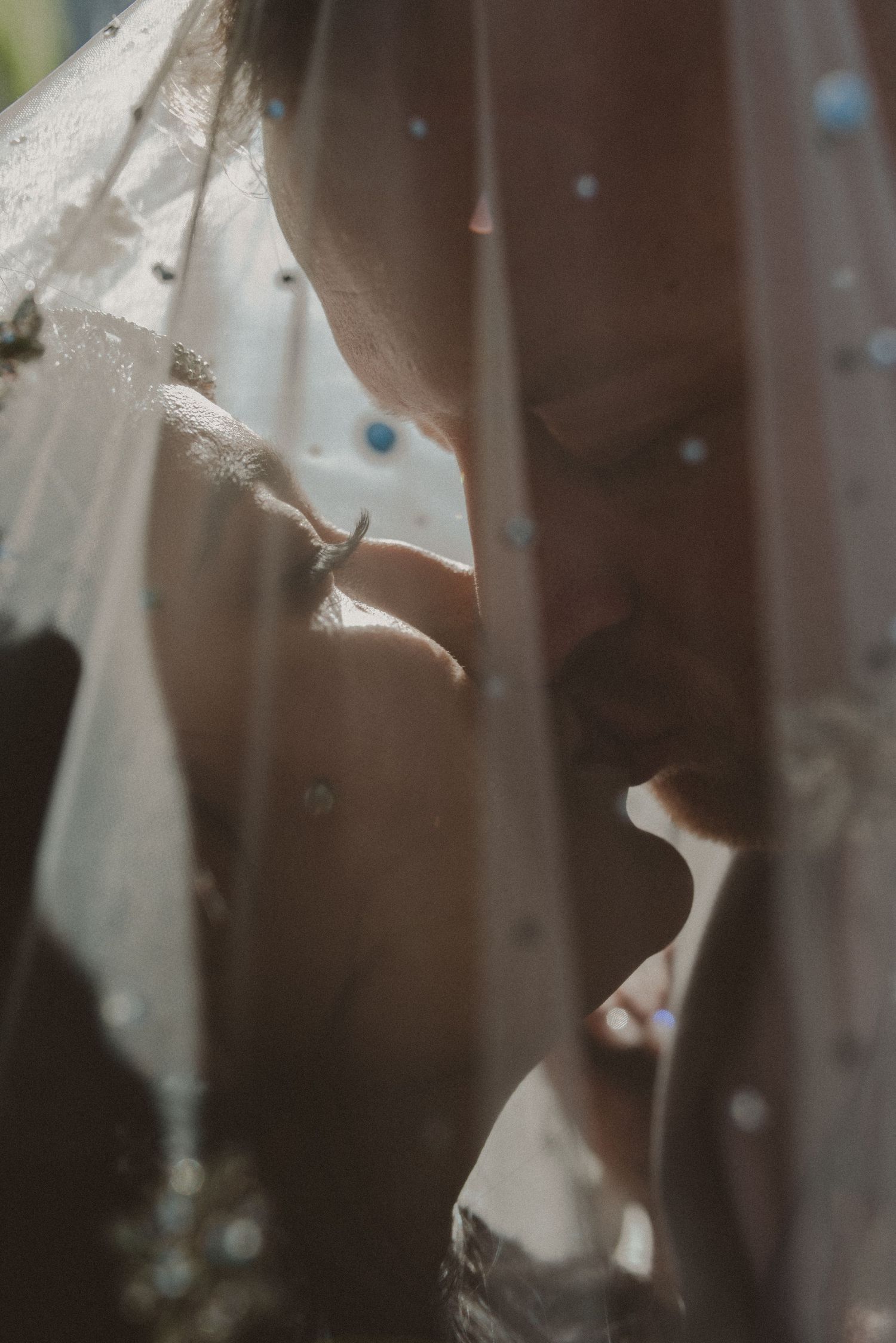 Romantic wedding couple kissing under a sheer veil with pearl details, bride wearing an elegant ring.