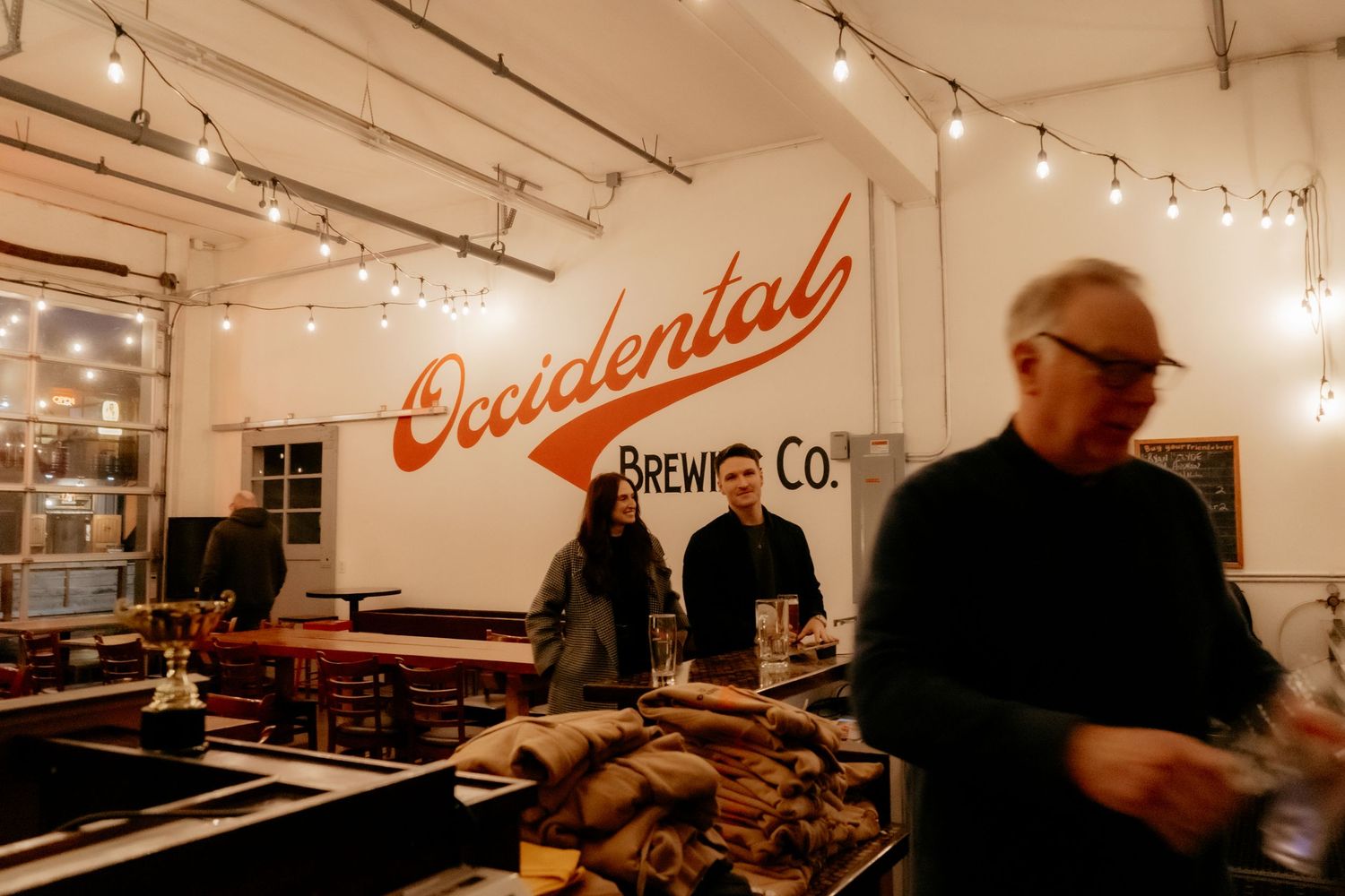 Interior of Occidental Brewing Co. with string lights, guests mingling, and rustic decor in Portland, Oregon.