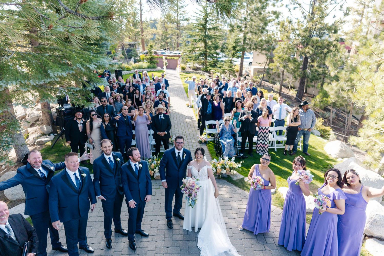 Bride and groom walk down the aisle surrounded by wedding party and guests at an outdoor ceremony.