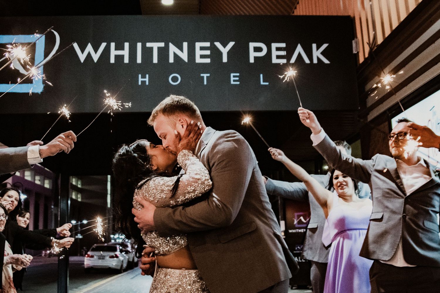 Couple sharing a first kiss under sparklers outside Whitney Peak Hotel during their wedding celebration at night.