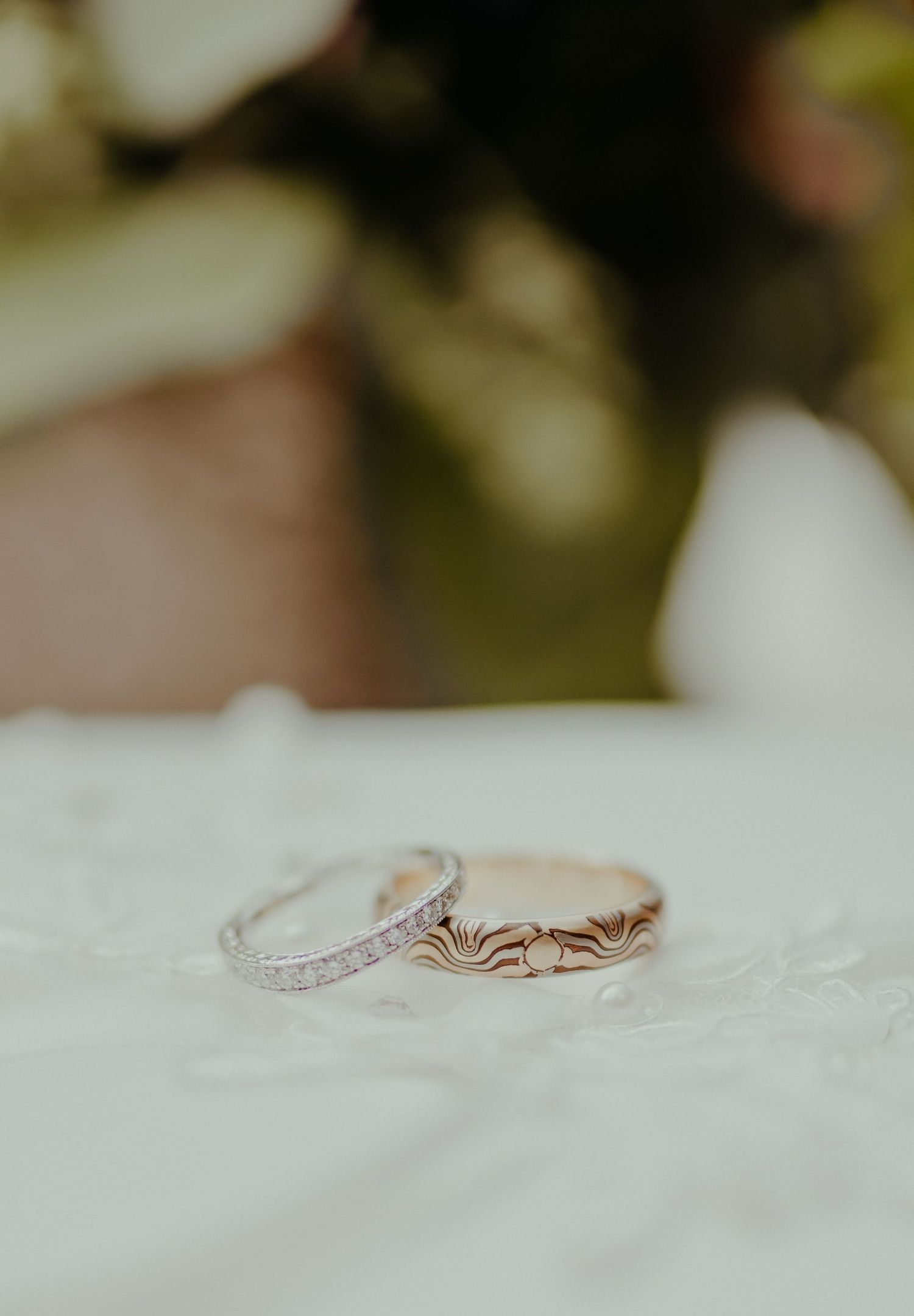 Two wedding rings, a diamond eternity band and rose gold engraved band, displayed on white lace fabric.