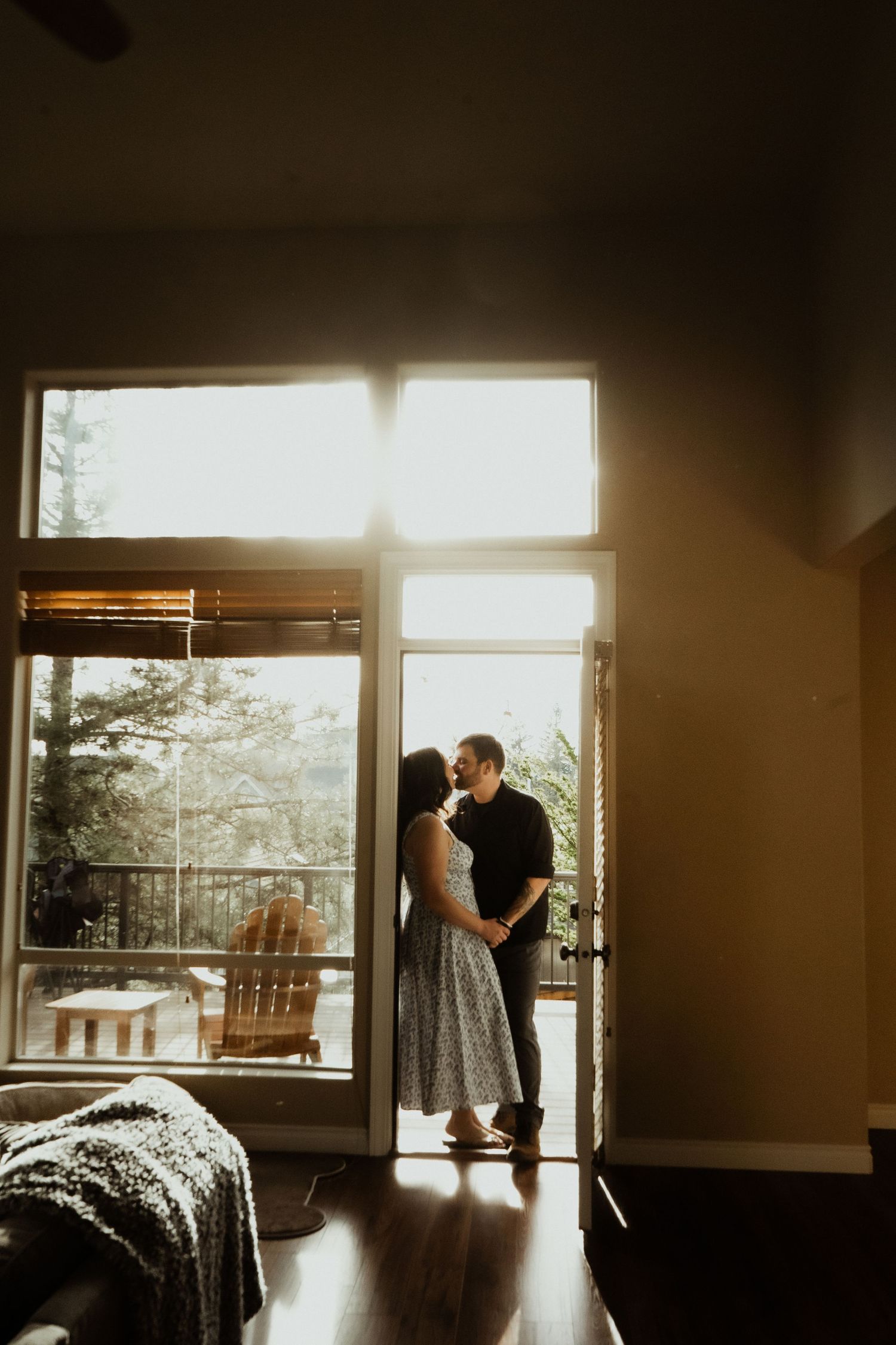 Couple sharing a romantic kiss silhouetted against a sunlit glass door in a warmly lit home.