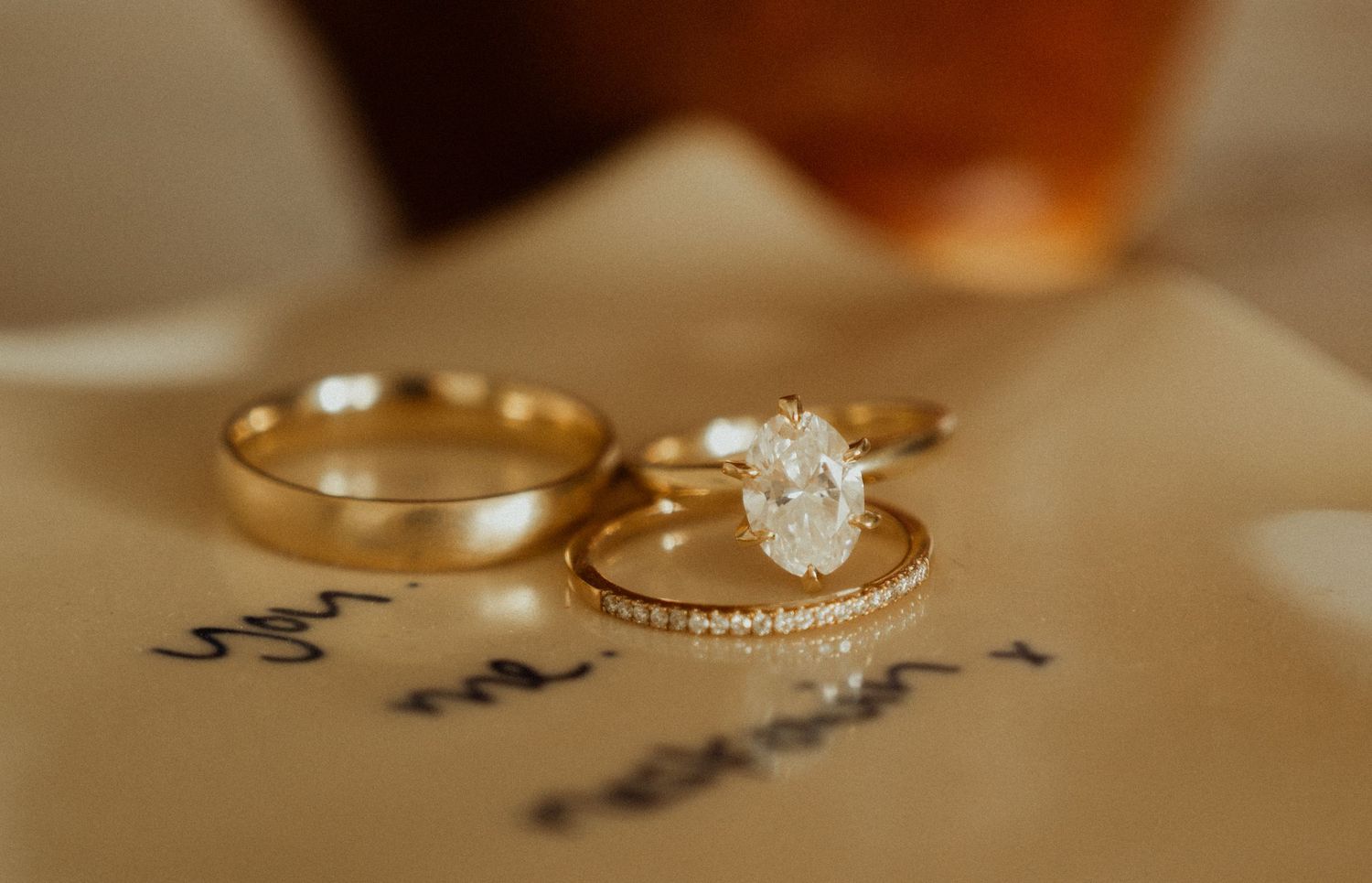 Gold wedding band and oval diamond engagement ring with pavé band resting on a handwritten vow card.