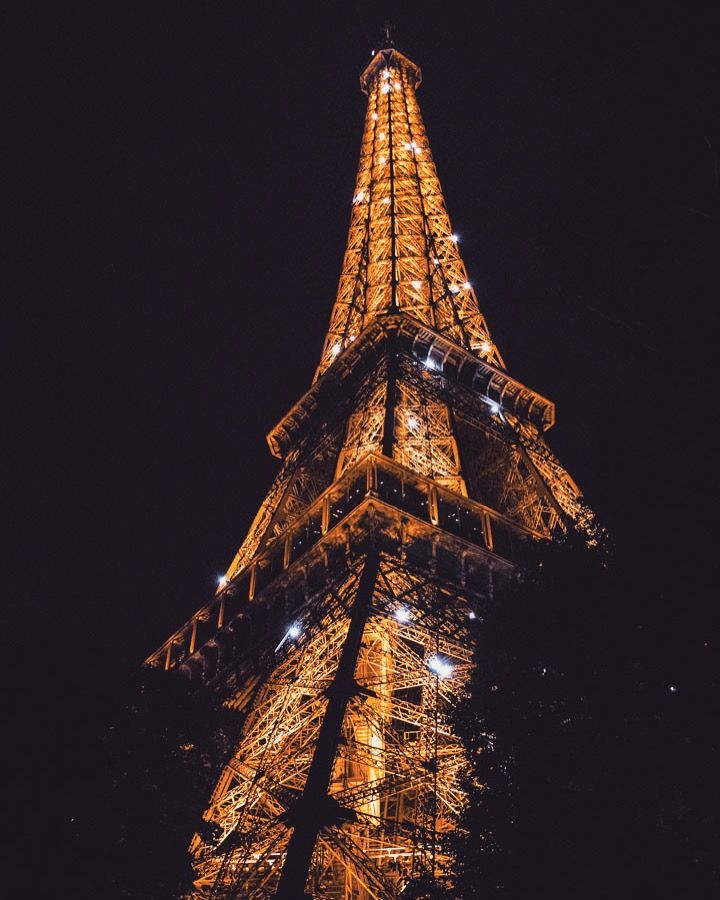 Dramatic low-angle night view of the illuminated Eiffel Tower glowing golden against a dark sky.
