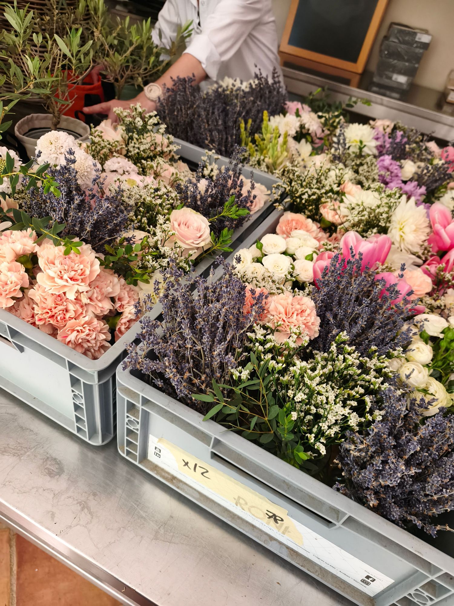 Florist workspace with crates of fresh lavender, pink roses, carnations, and white blooms for event floral arrangements.